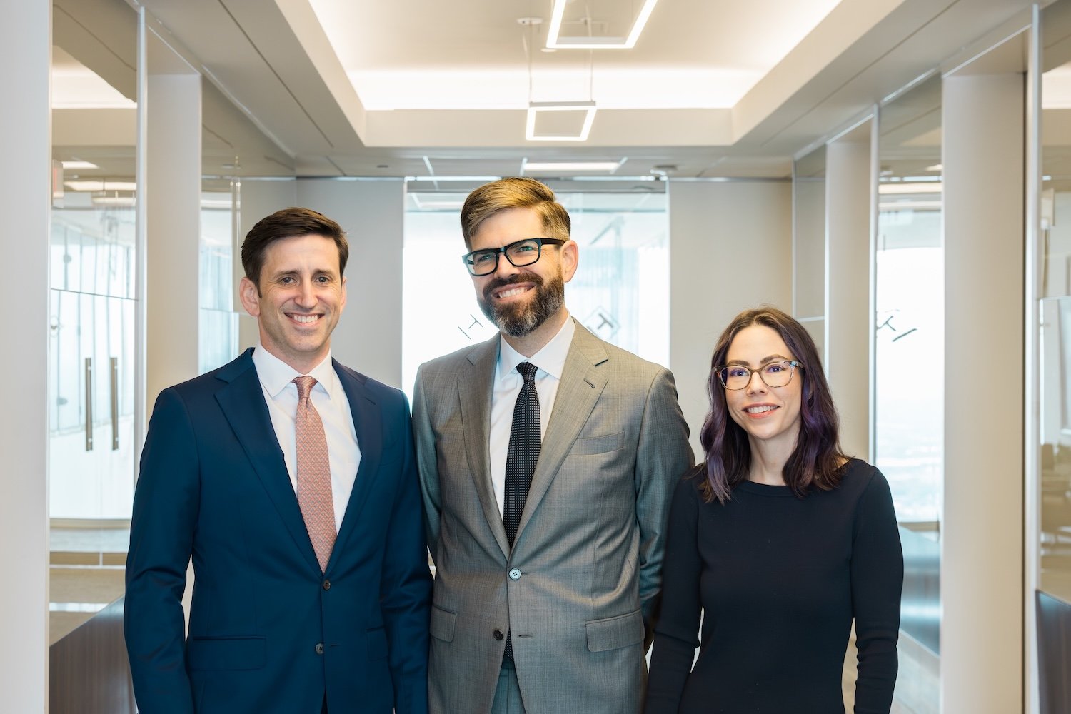 James Schuelke, Christopher Hogan, and Samantha Thompson smiling and standing in the hallway at Hogan Thompson Scheulke's downtown Houston law firm offices.