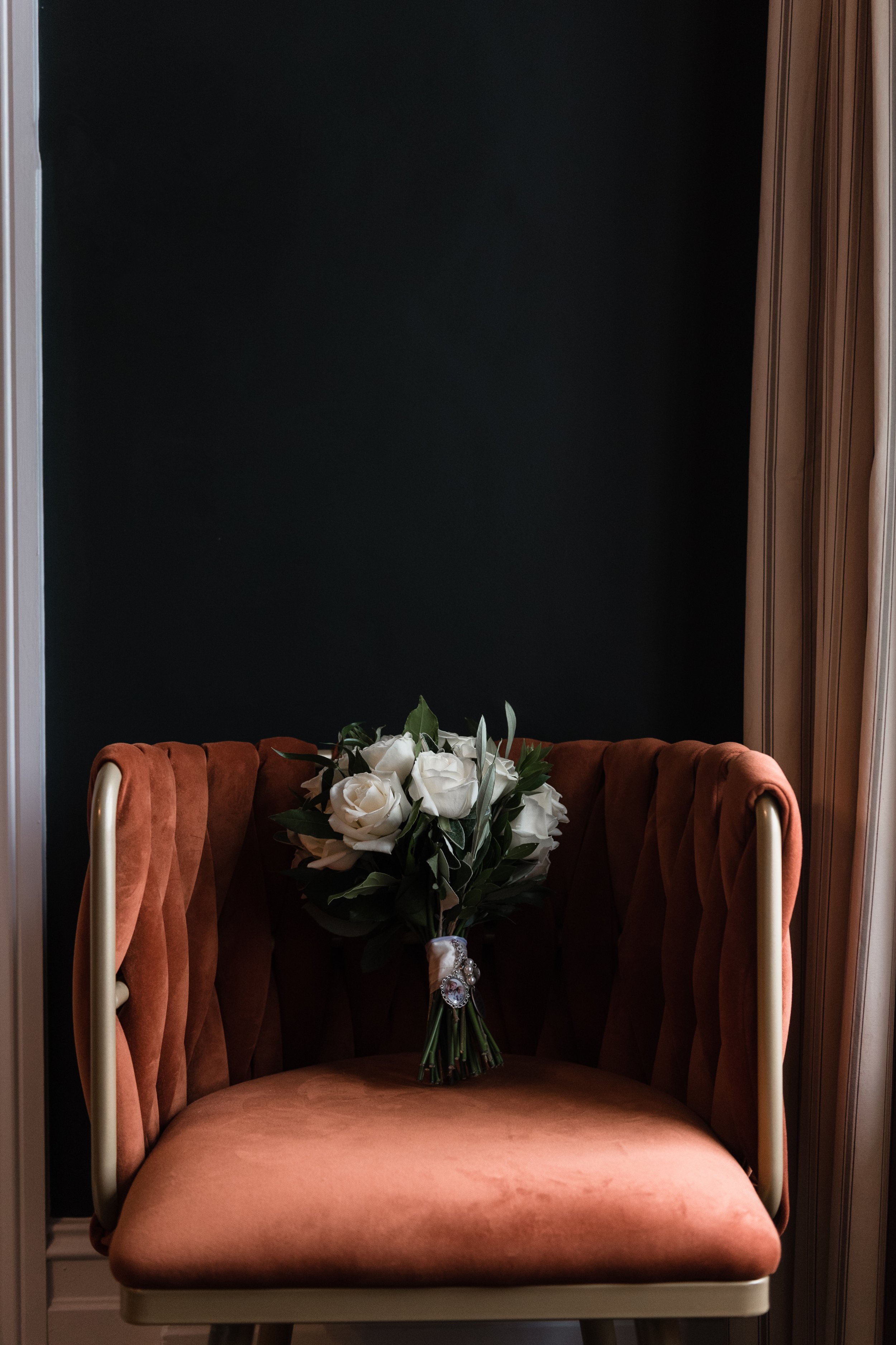 Orange velvet chair with white rose bouquet against dark wall background