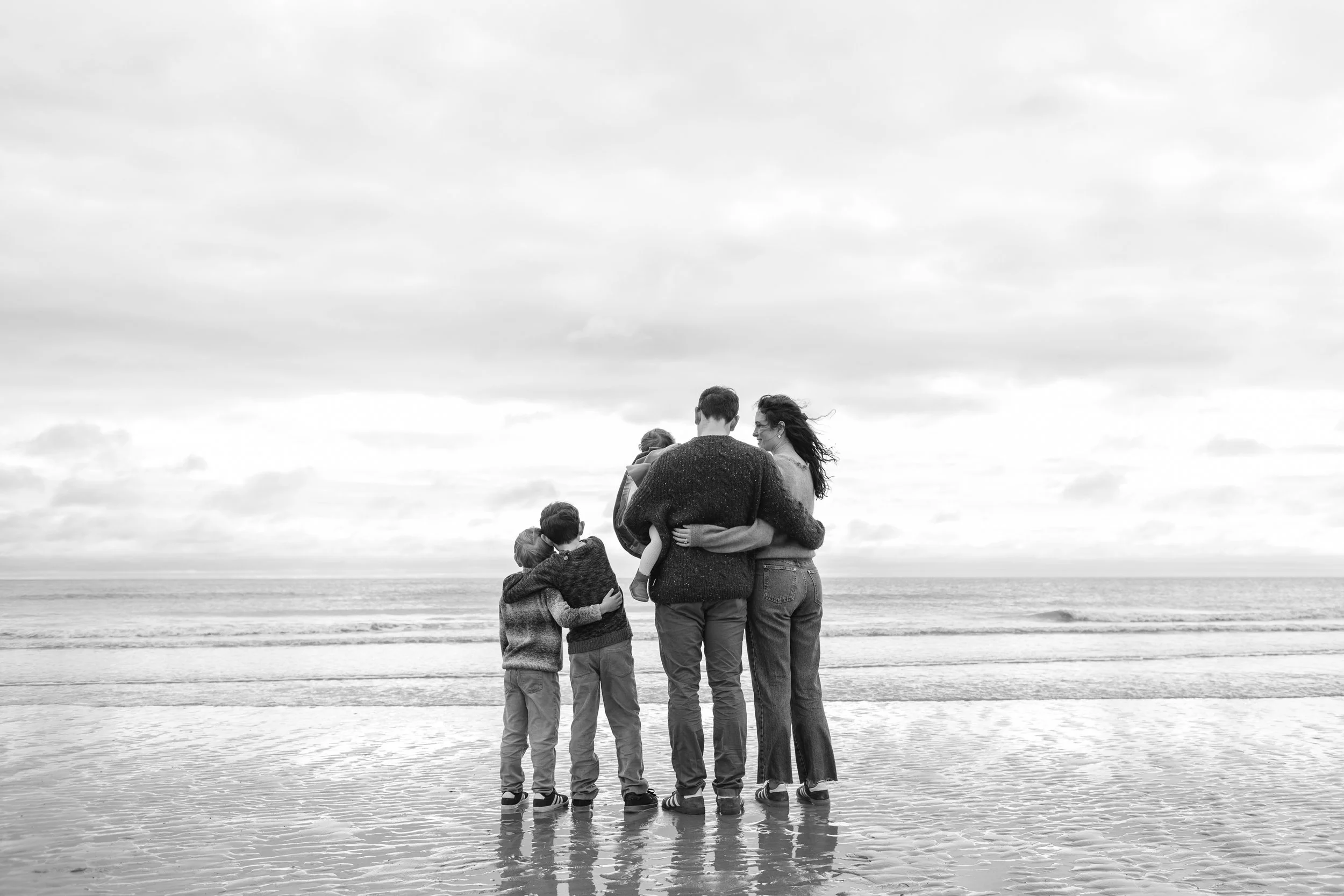 black and white photo of a family on a beach facing the sea