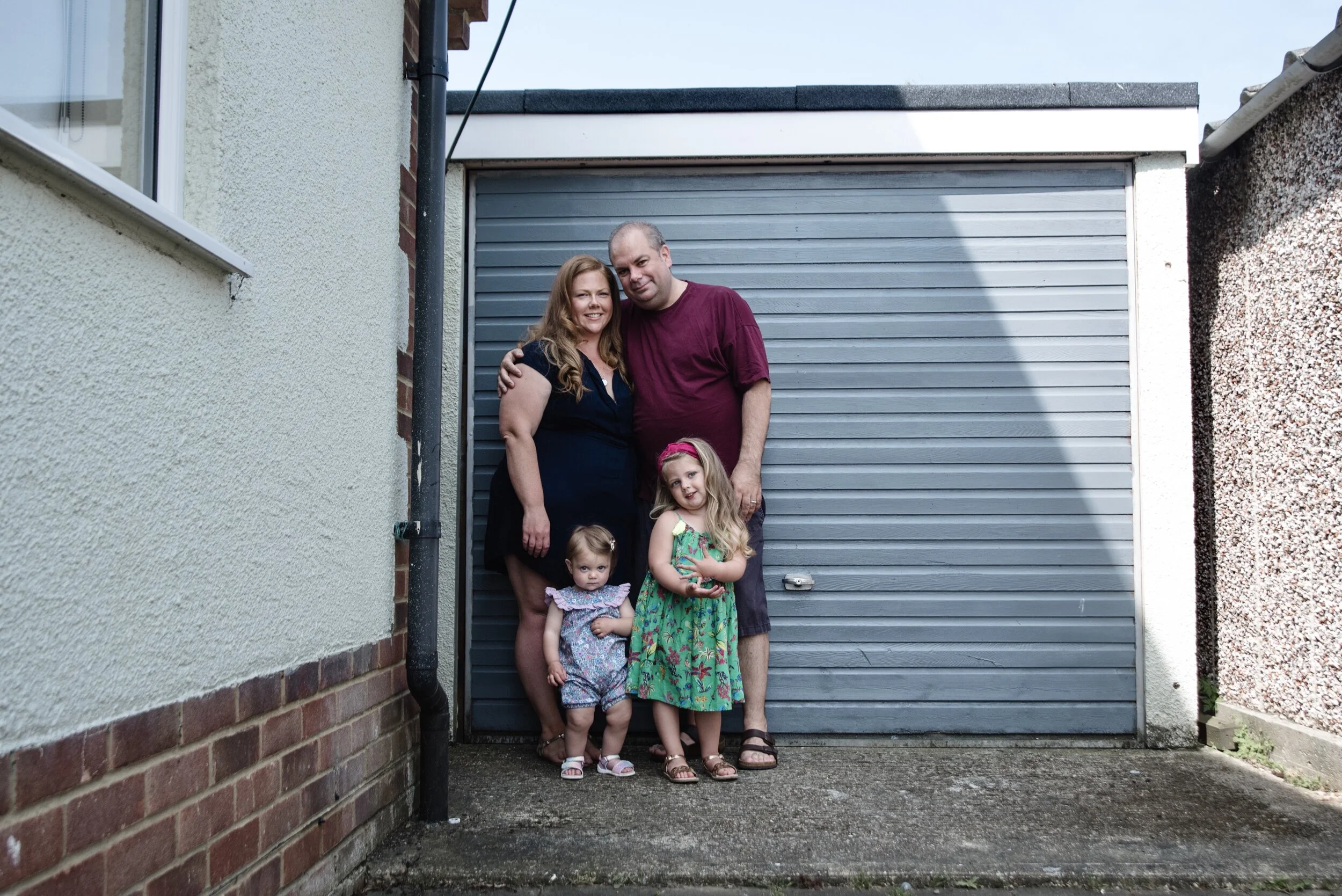 Family of four standing in front of a garage door, including a man, woman, and two young children, with surrounding walls.