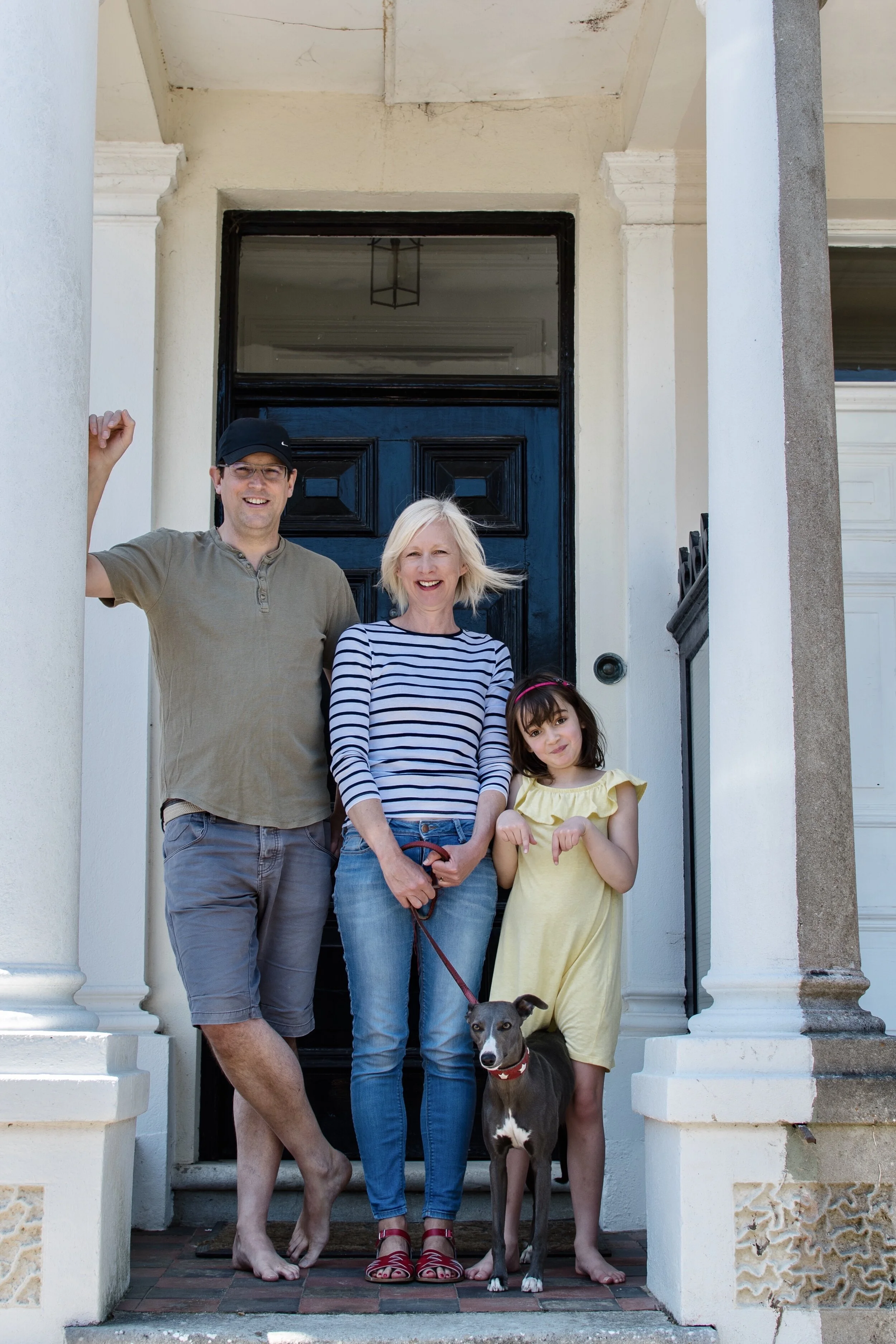 Family standing on front porch, smiling, with a small dog on a leash.
