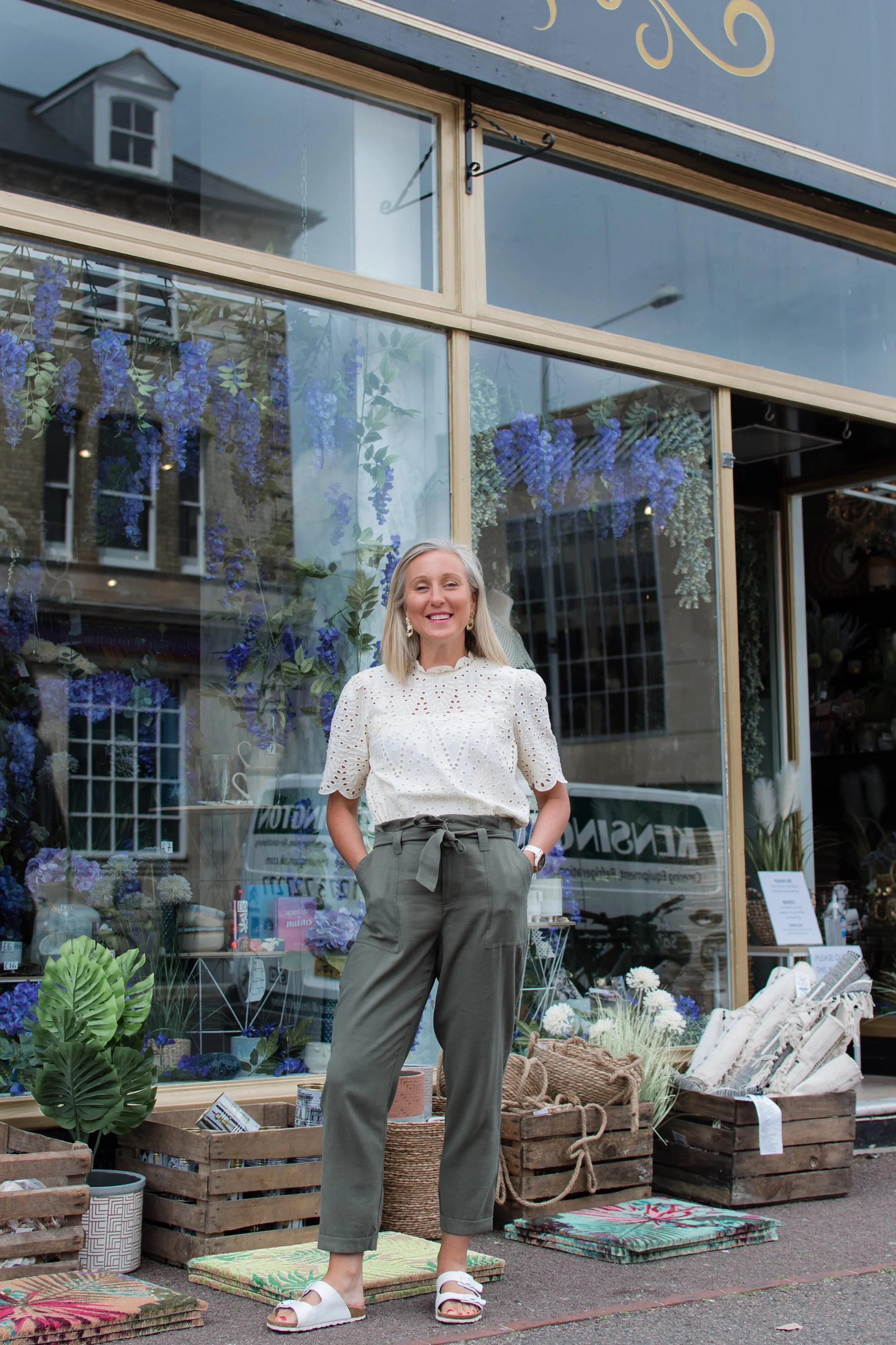 Woman standing in front of a decorated shop with plants and colorful items on display.