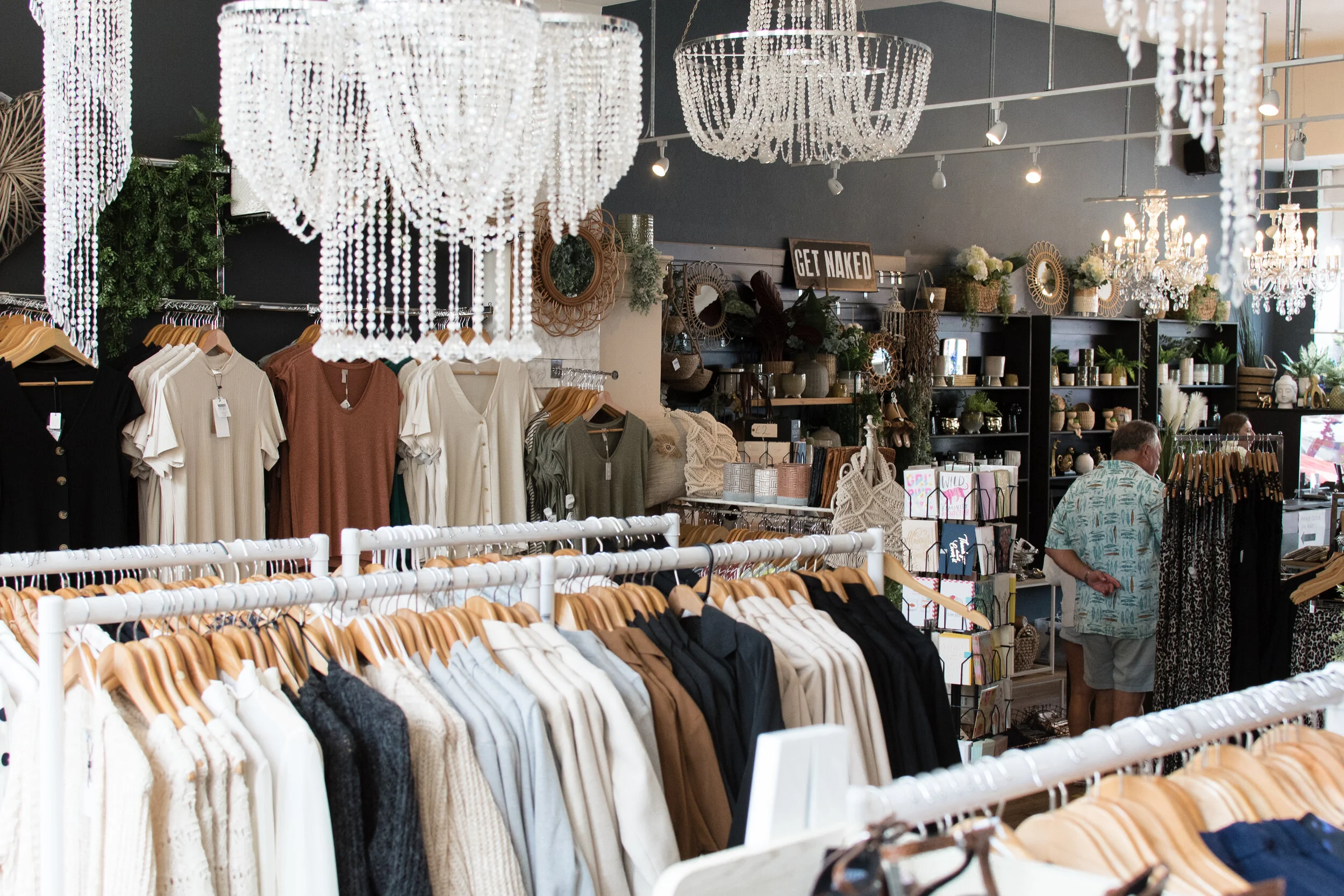 Clothing boutique interior with hanging chandeliers, racks of clothes, and decorative items on shelves.