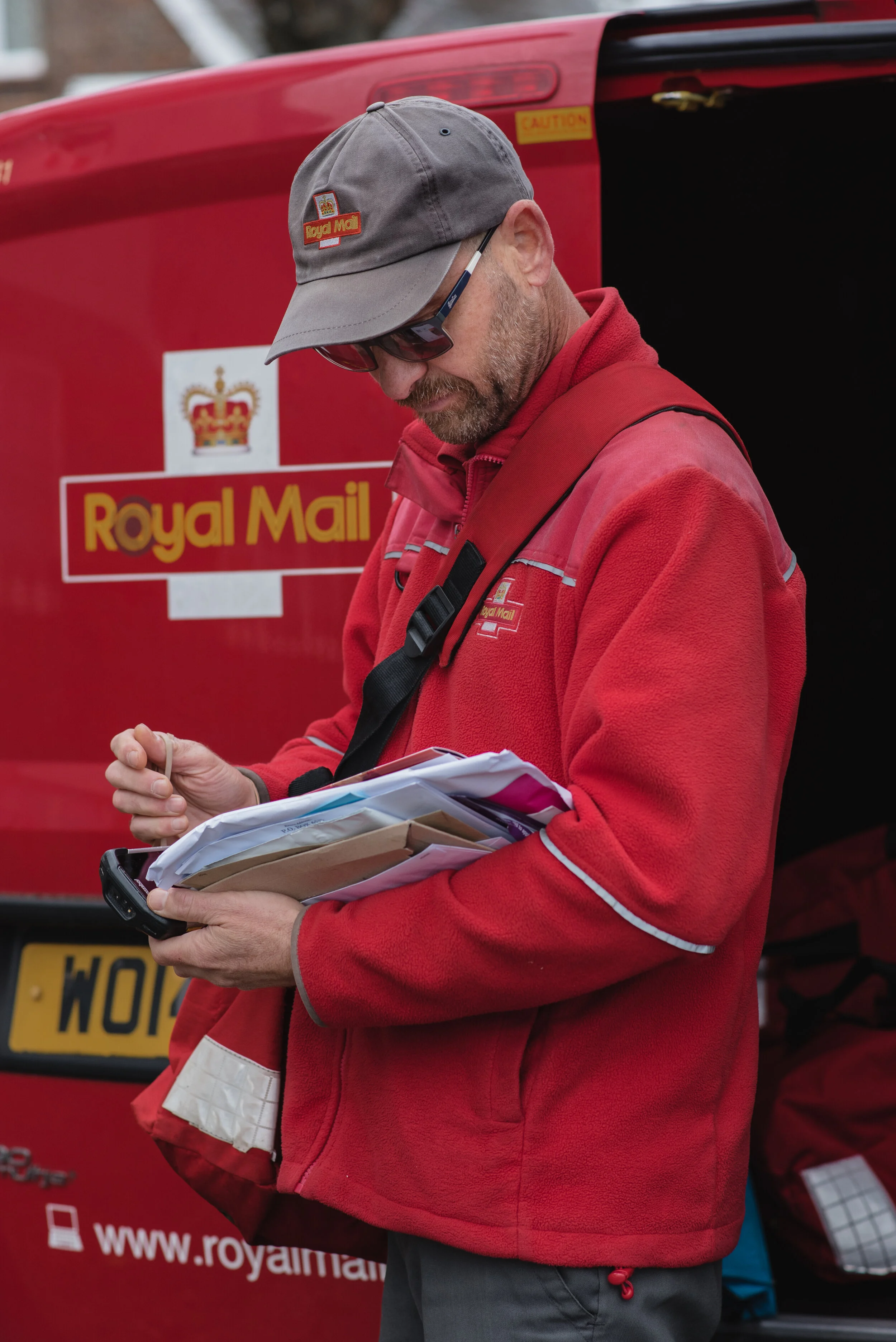 Royal Mail worker in red uniform sorting mail near van