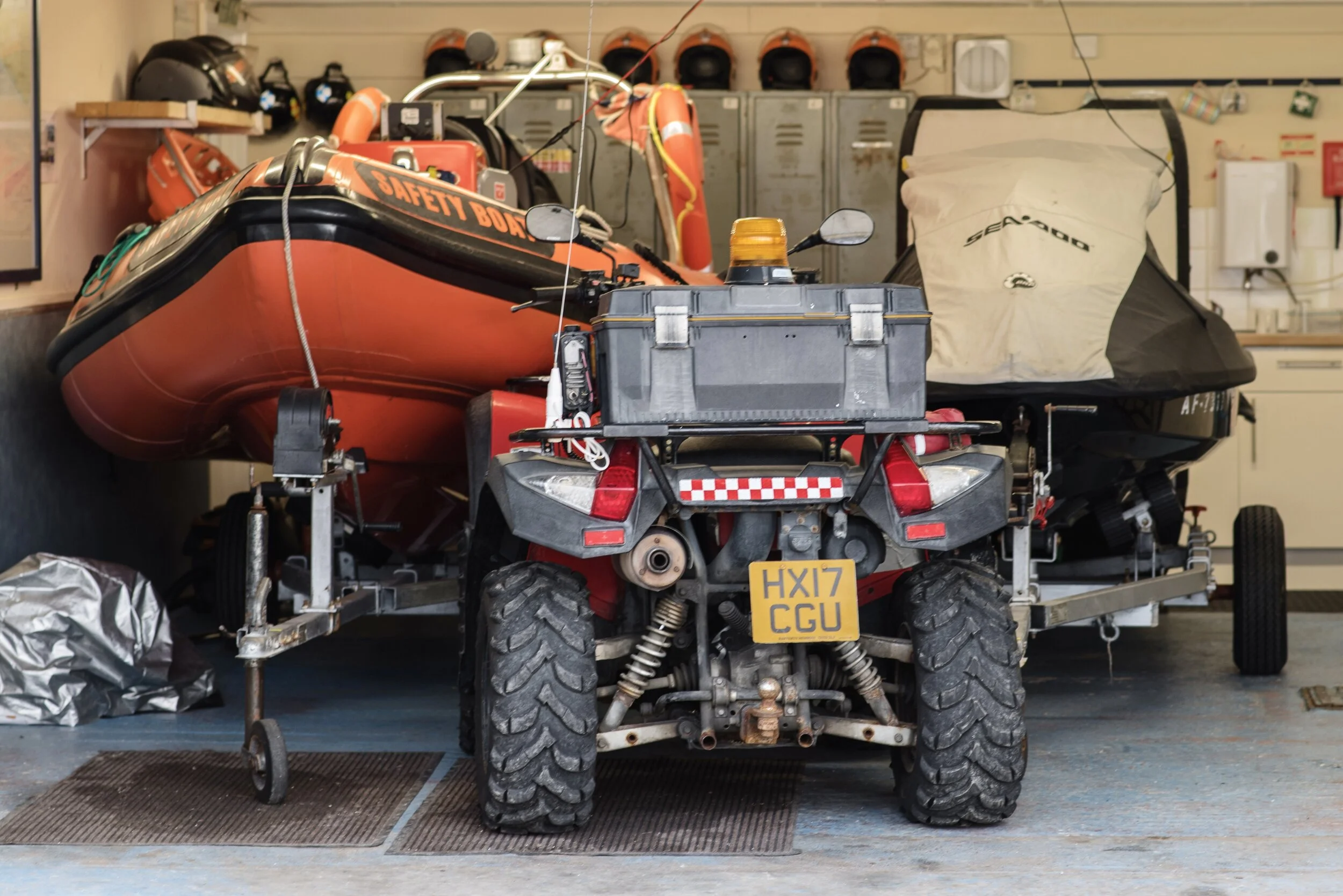 A garage with an ATV and two boats, including an orange safety boat and a covered jet ski.