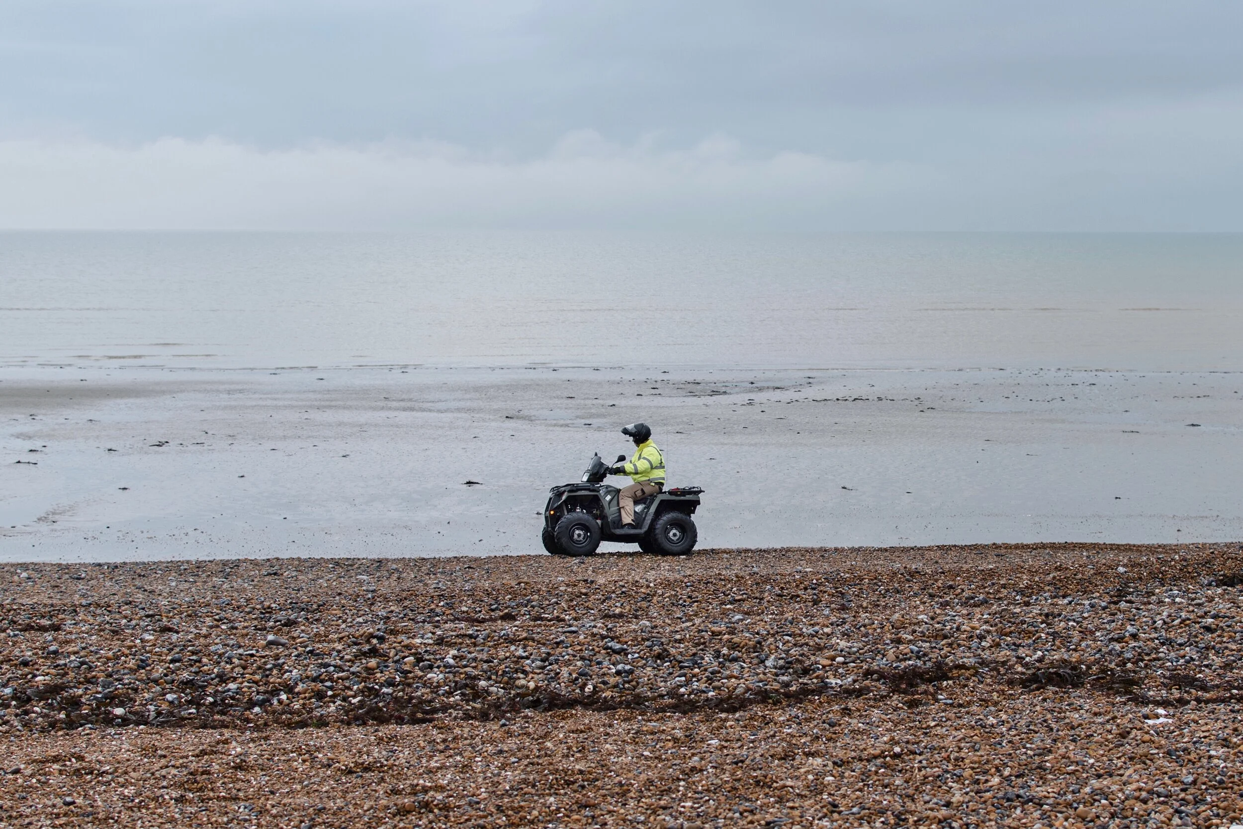 Person riding an ATV on a rocky beach near the sea under a cloudy sky.