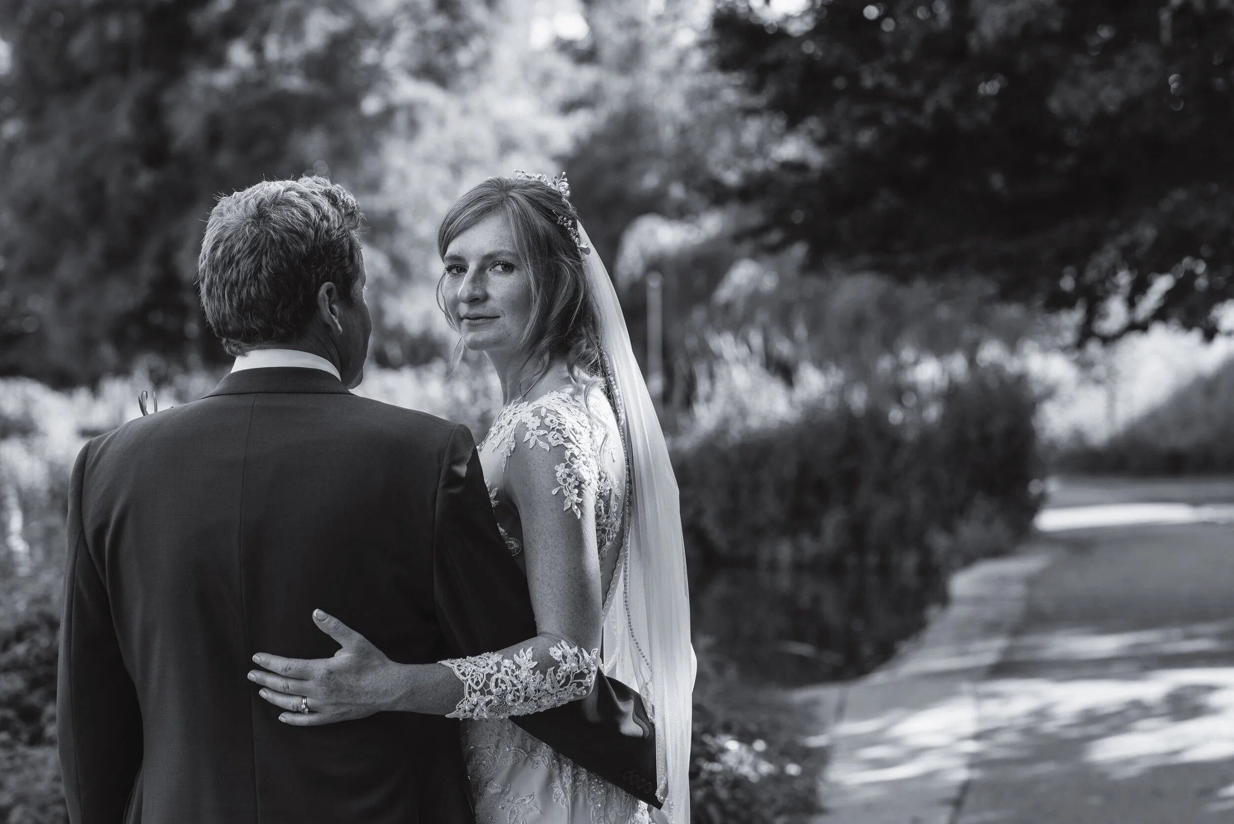 Bride and groom in black and white wedding photo walking on path