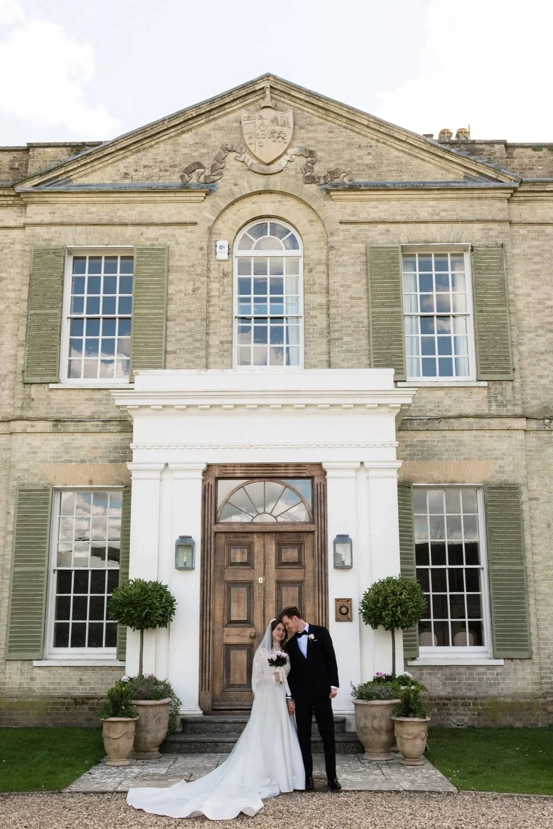 bride and groom standing against a manor house in Sussex