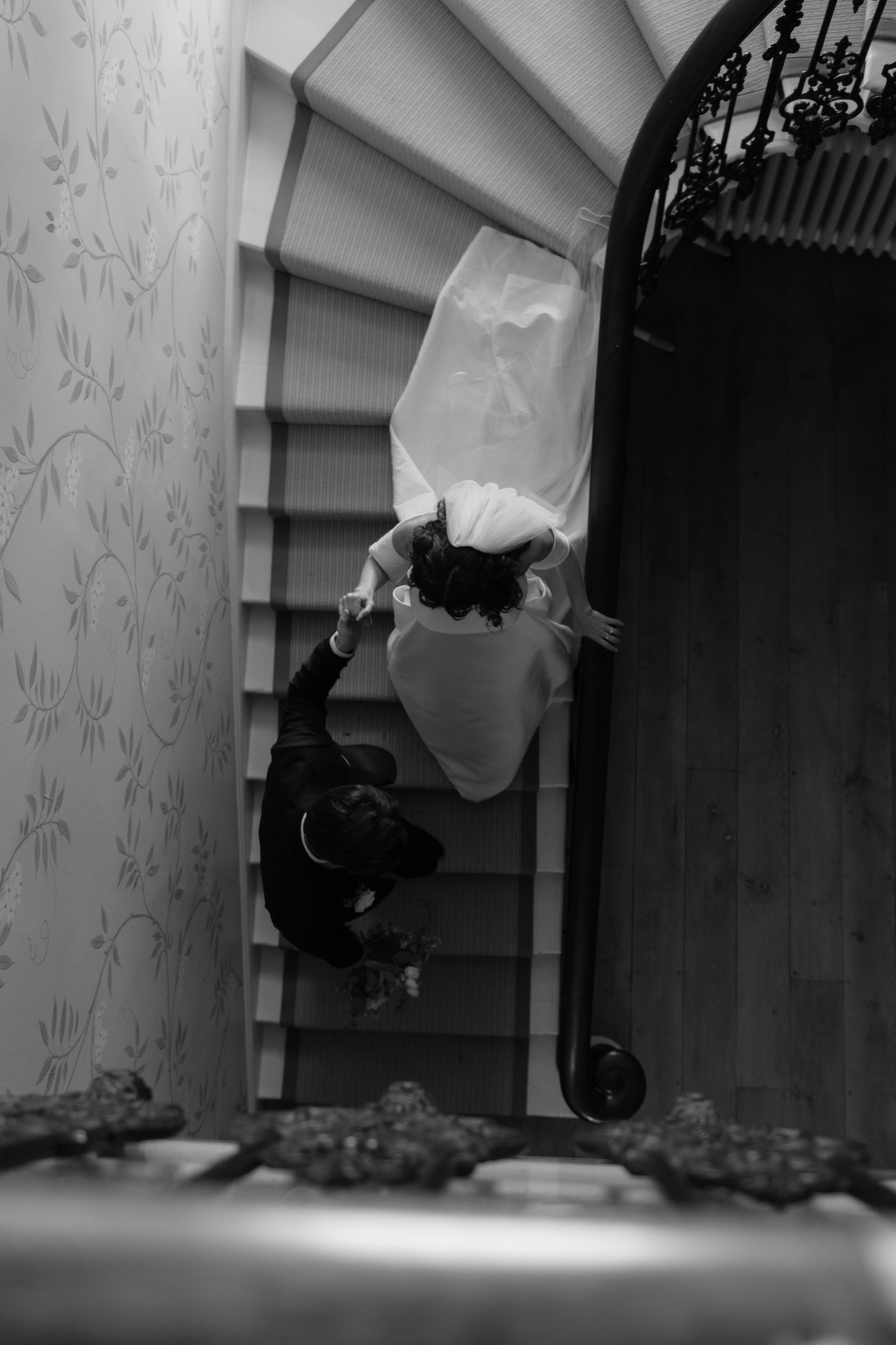 Bride and groom descending a spiral staircase, captured from above in black and white.
