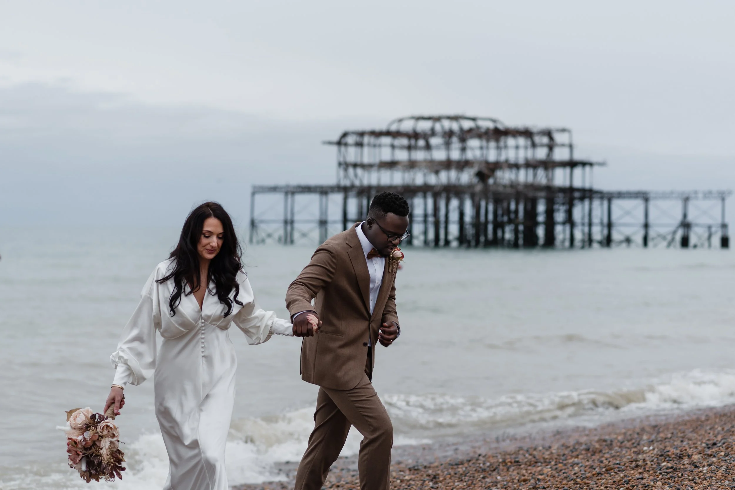 bride and groom on the beach in front of an old pier Brighton
