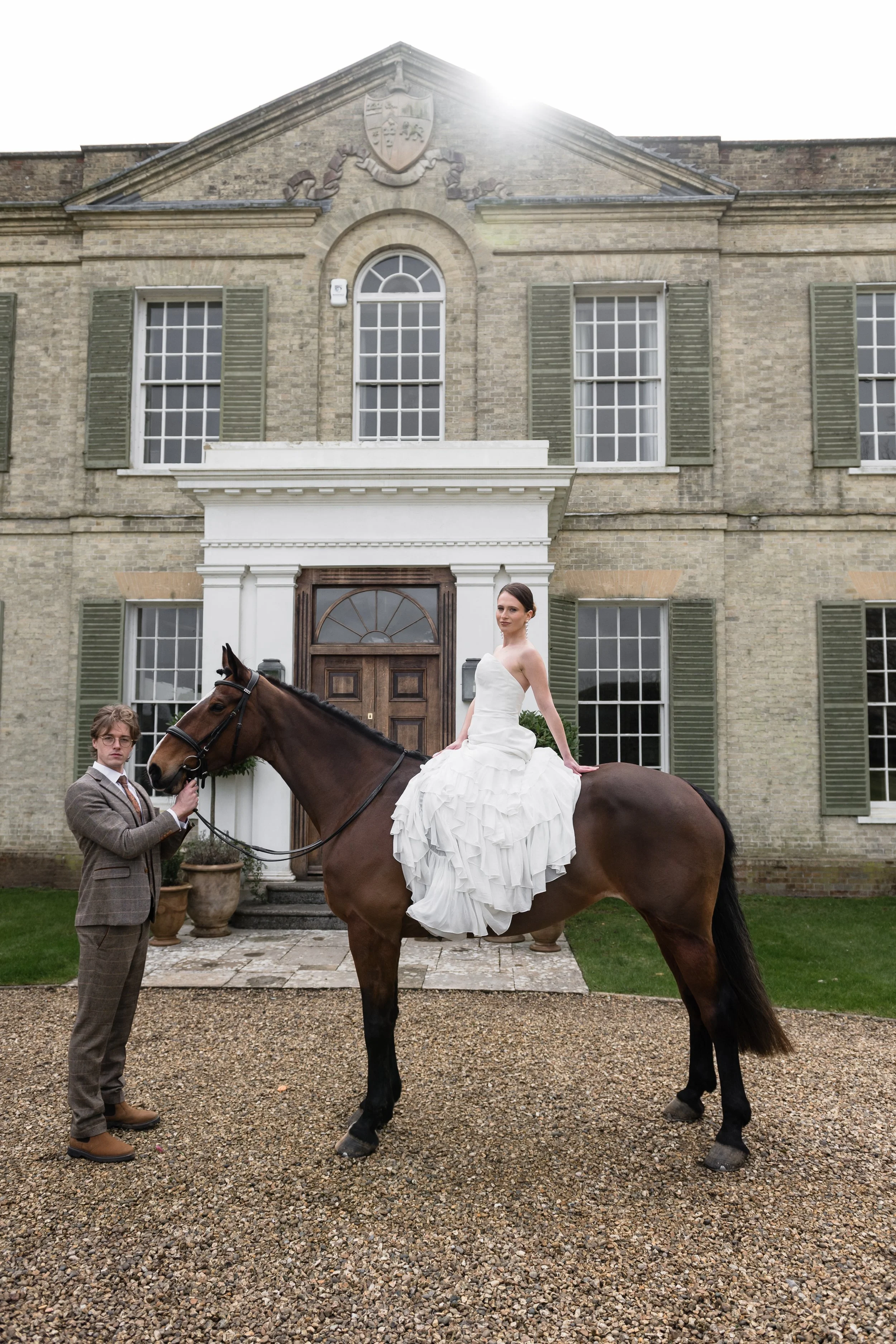 bride and groom with a horse standing against a country 
manor house