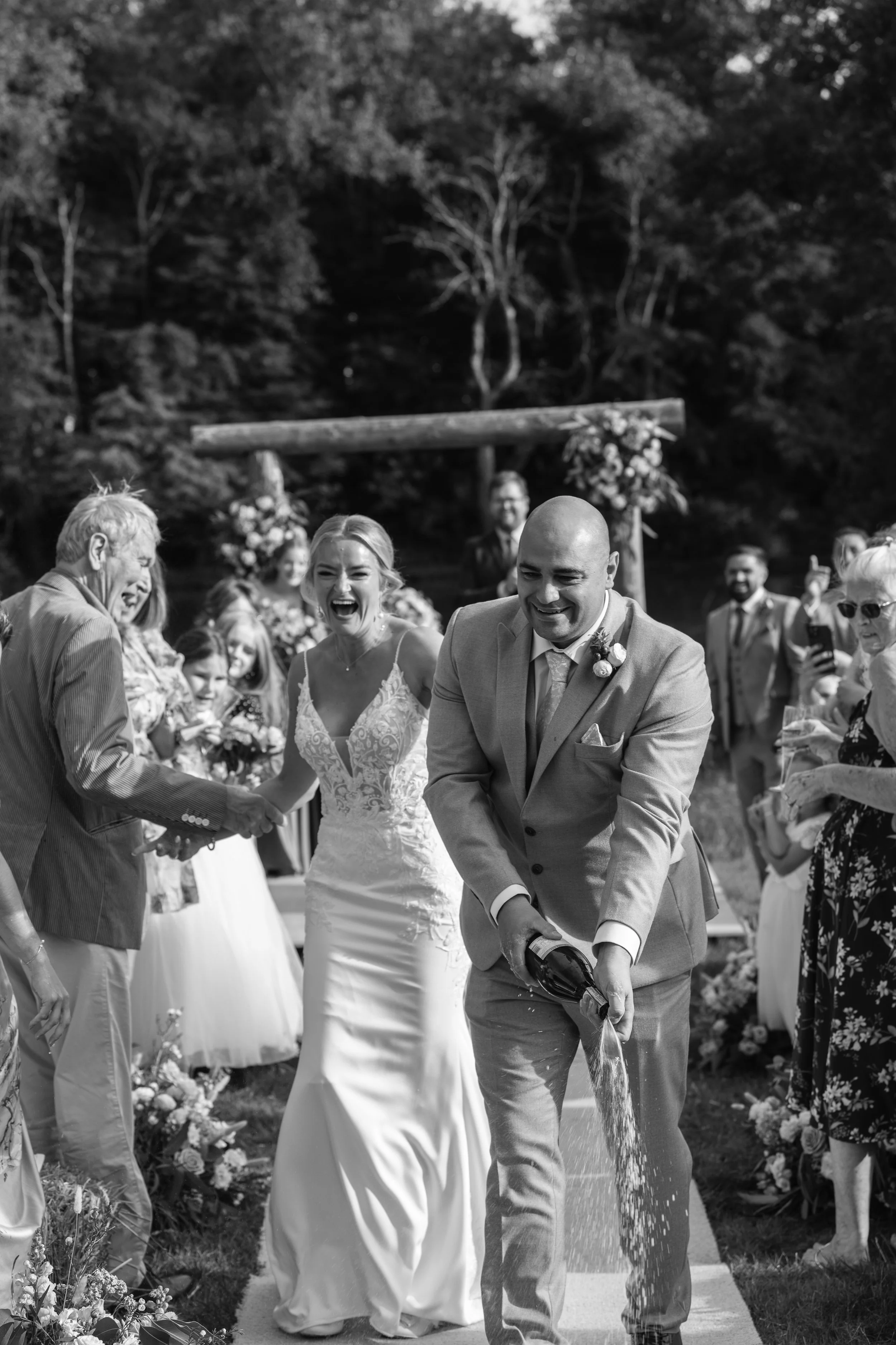 Black and white image of a bride and groom spraying champagne