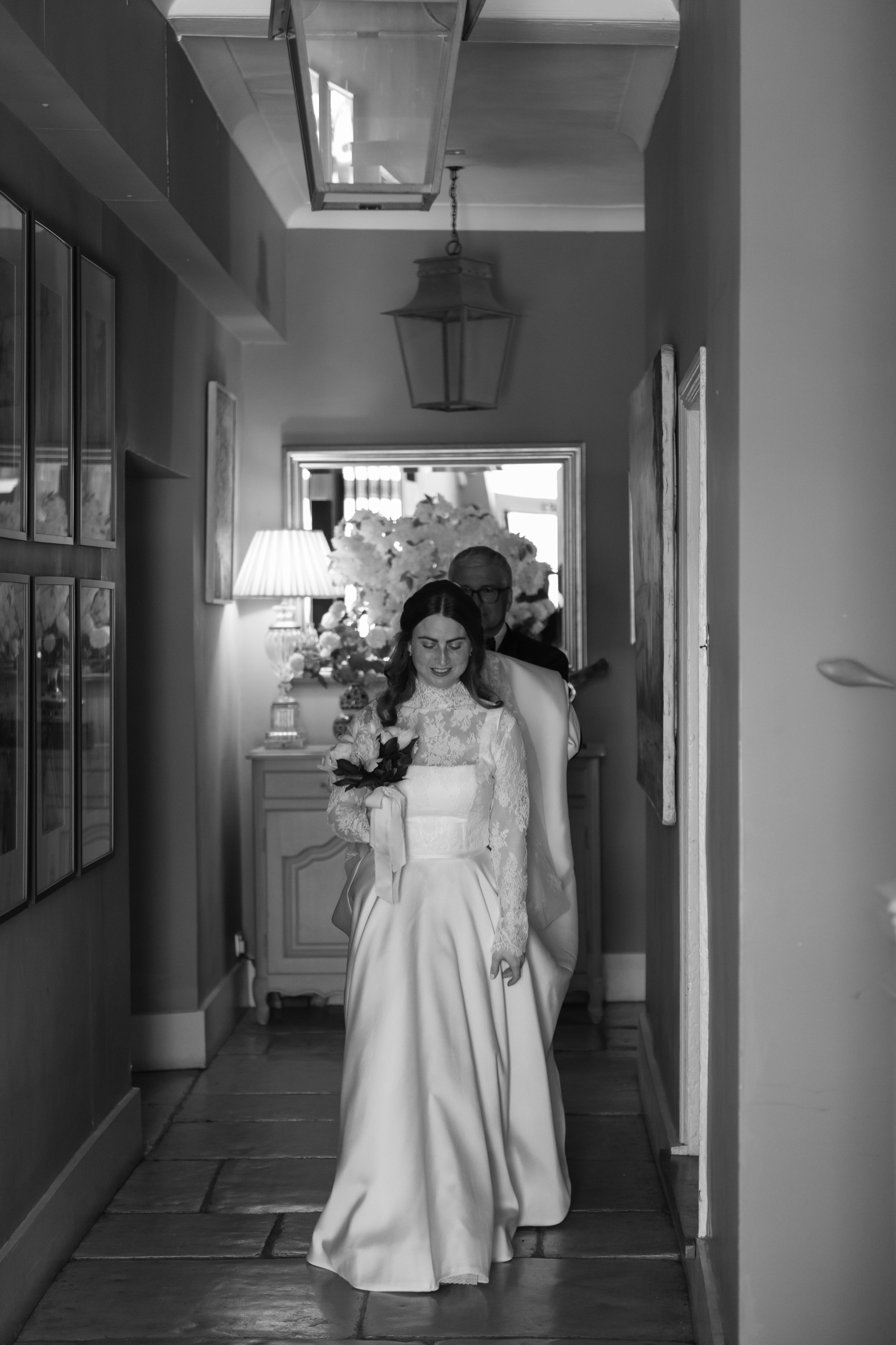 bride walking in a manor house hallway with her dad holding her dress