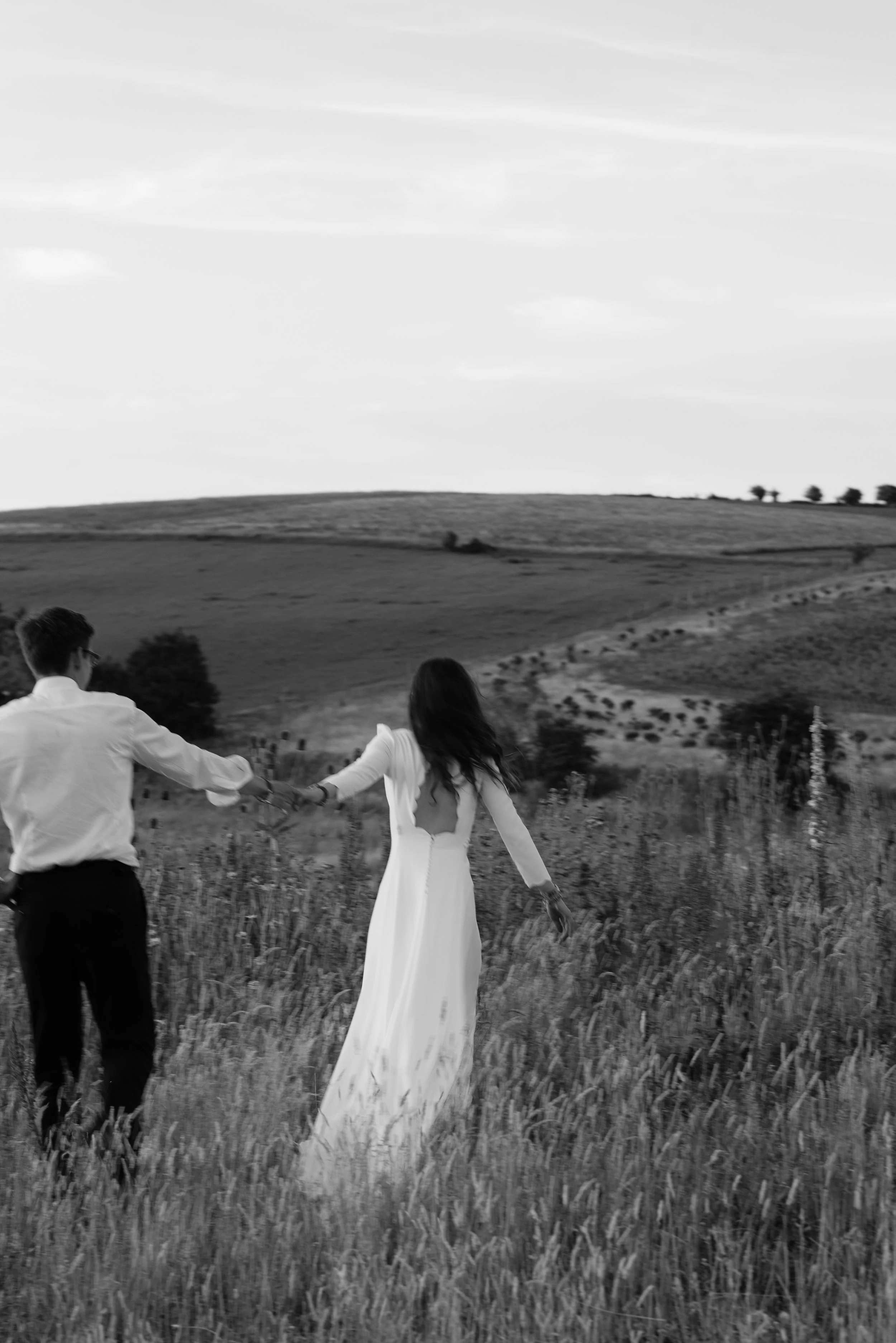 Black and white photo of a bride and groom walking through a field at a wine estate 