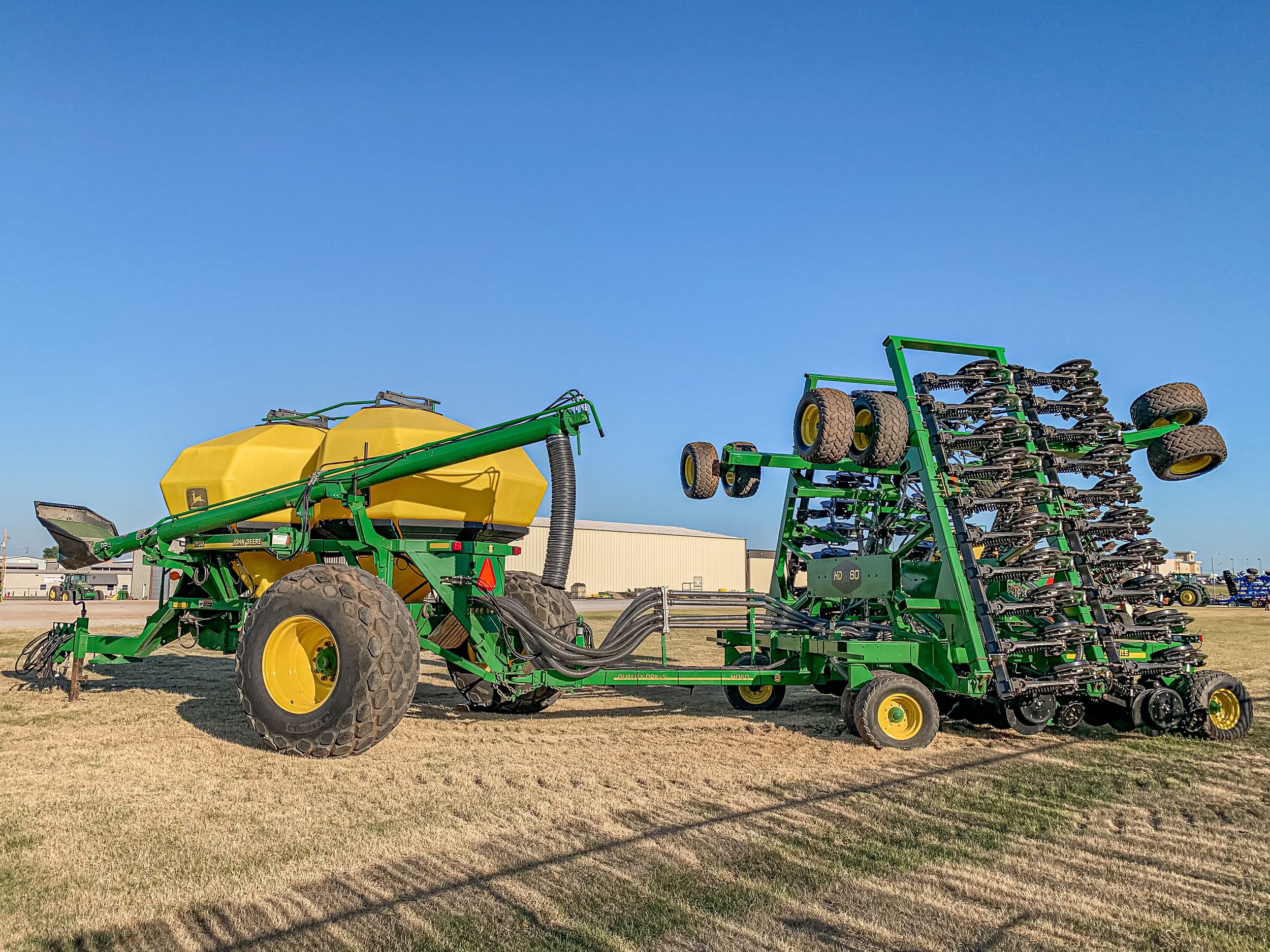 Large green John Deere agricultural machinery with a yellow tank and multiple tires, set on a grassy field under a clear blue sky.