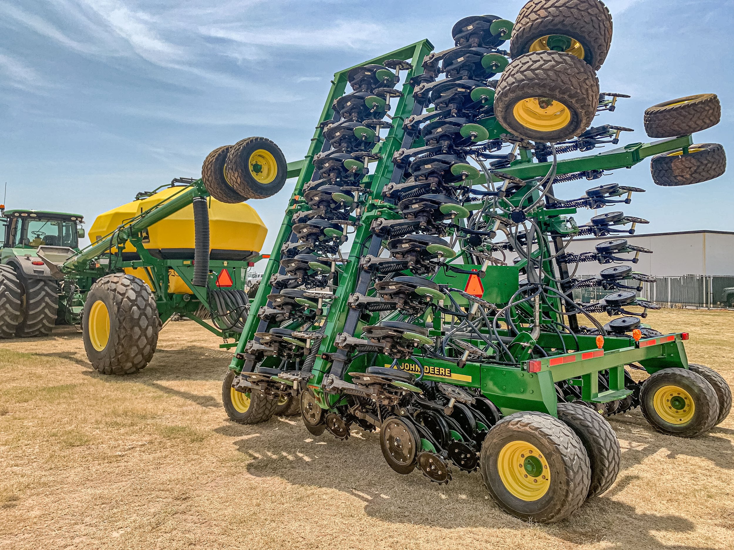 Large green and yellow John Deere agricultural planter with multiple rows of disc openers and tires, on a farm field.