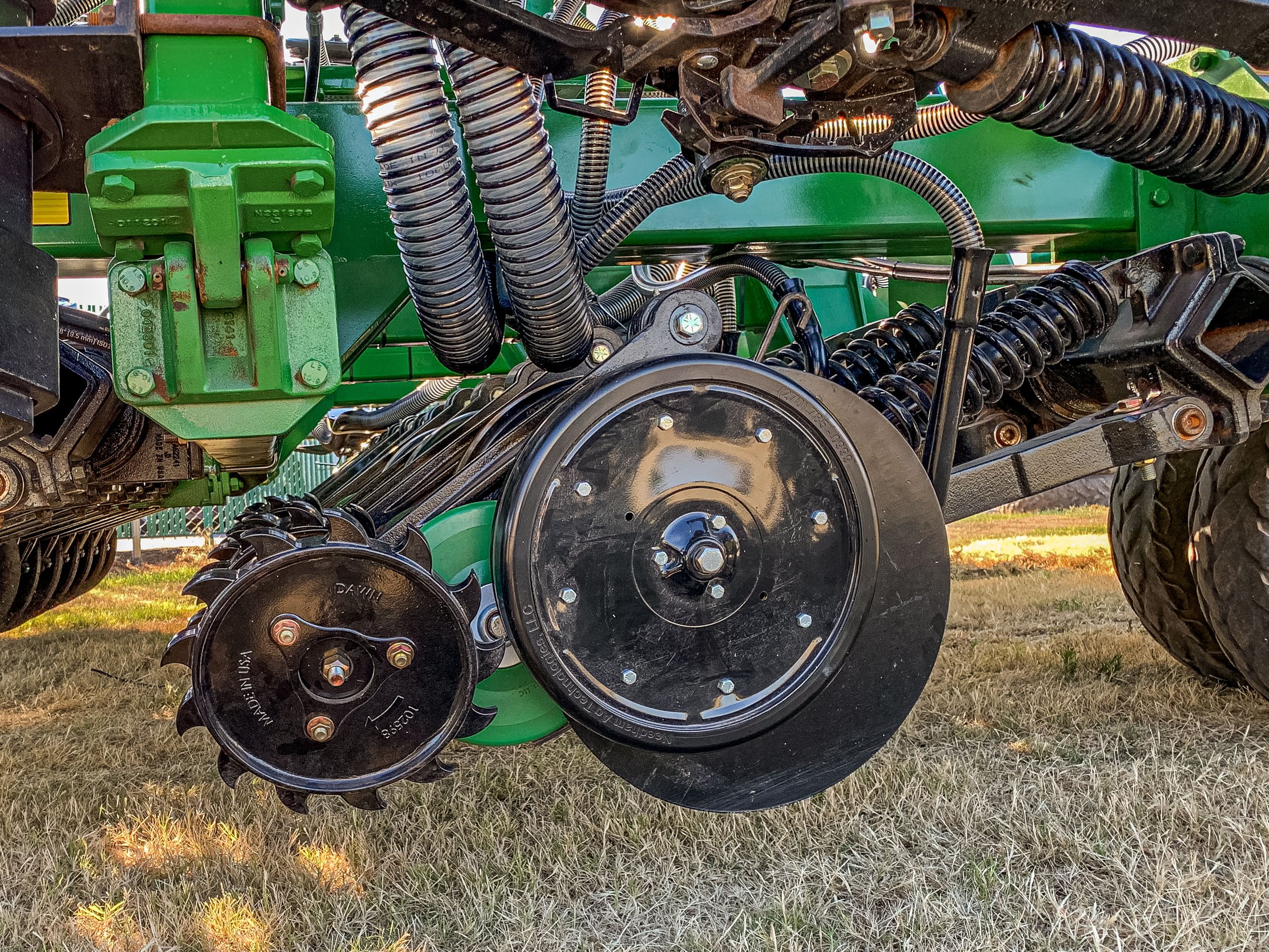 Close-up of an agricultural machine component showing green and black parts, coils, and gears on a grassy surface.