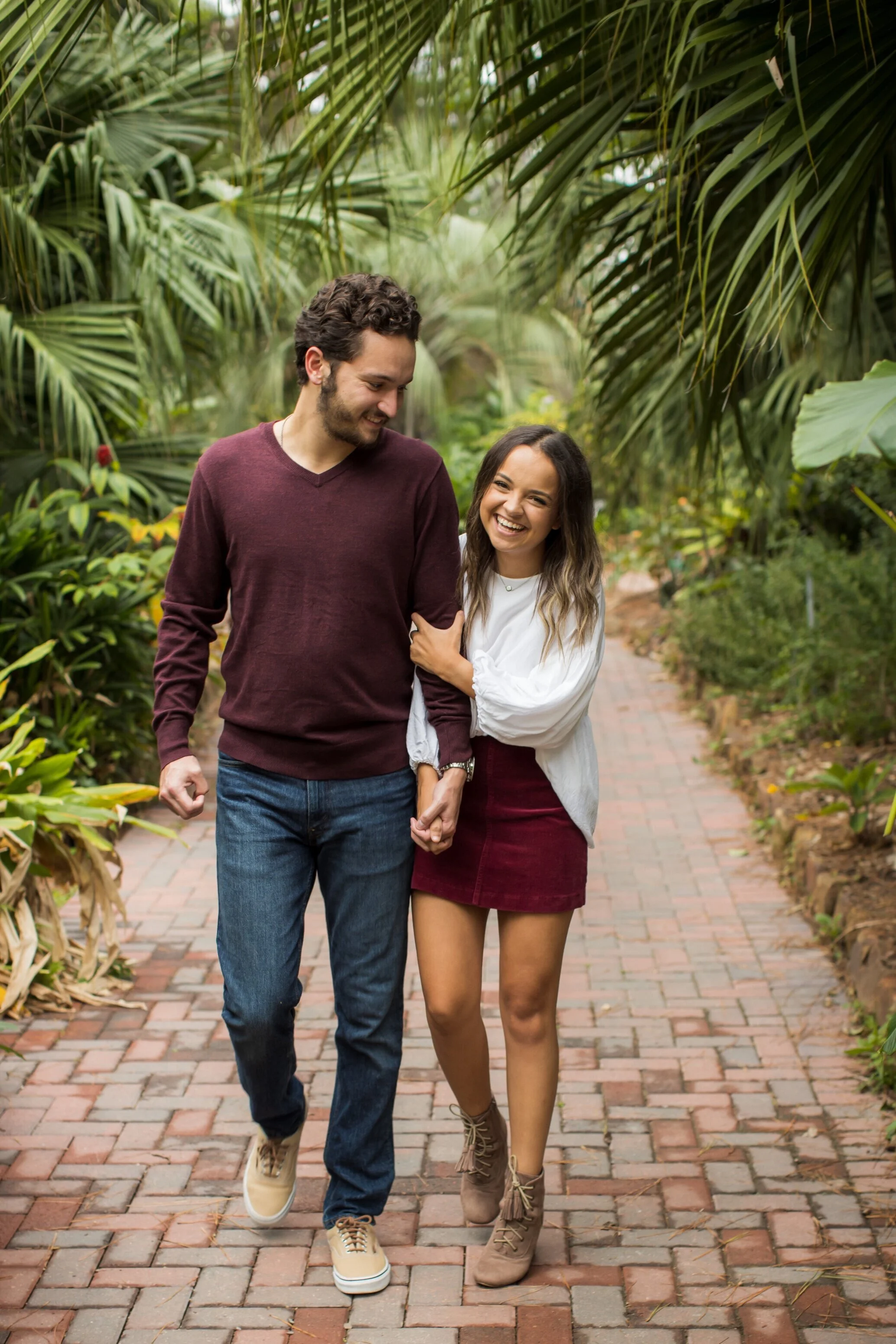 A young man and woman walking hand in hand through a lush garden, smiling and enjoying each other's company.