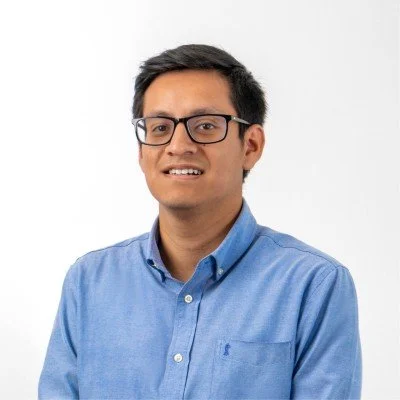 Portrait of a man wearing glasses and a blue button-up shirt, smiling, against a white background.