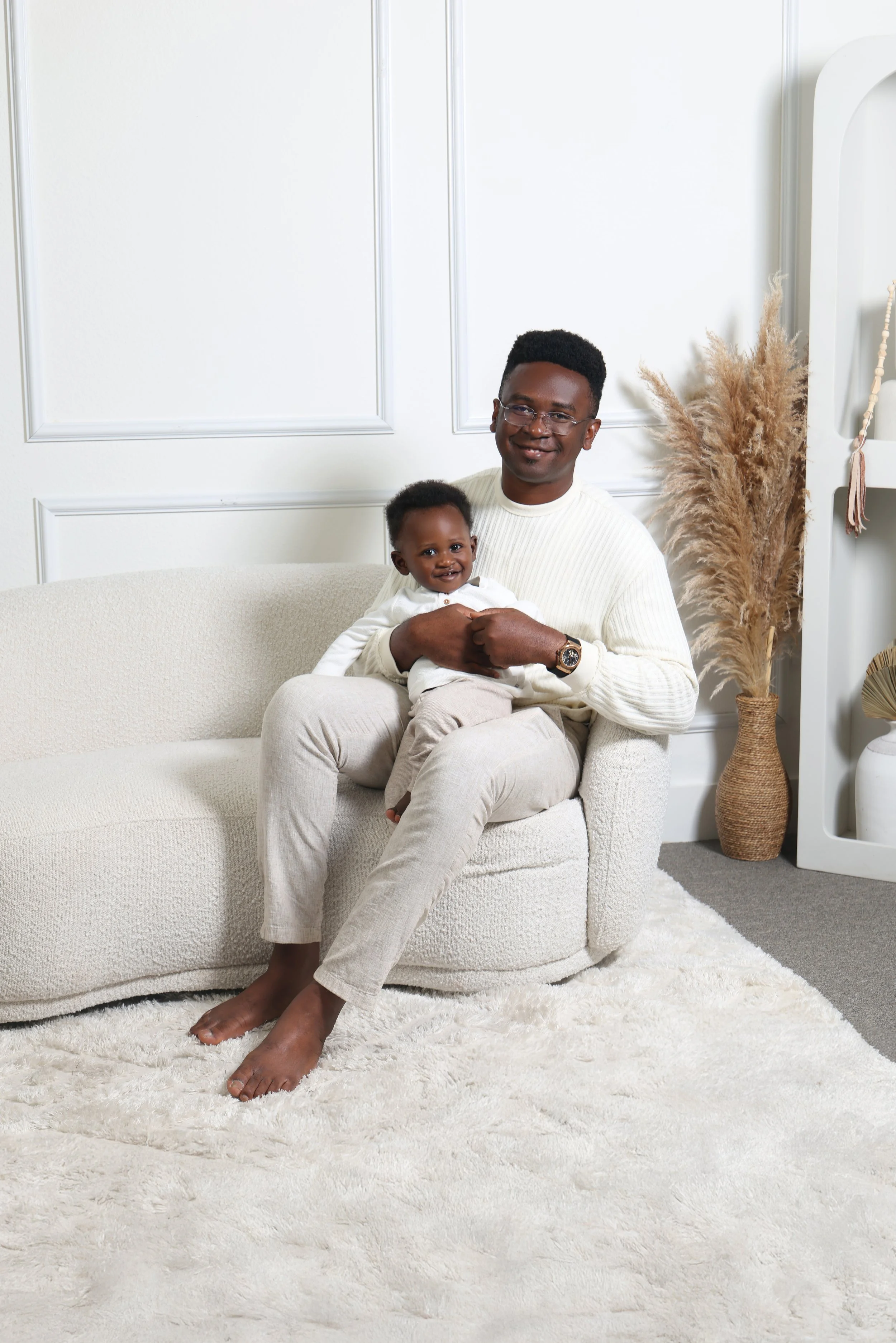 A man sitting on a cream sofa holding a smiling young child in a cozy room decorated with beige and white accents.