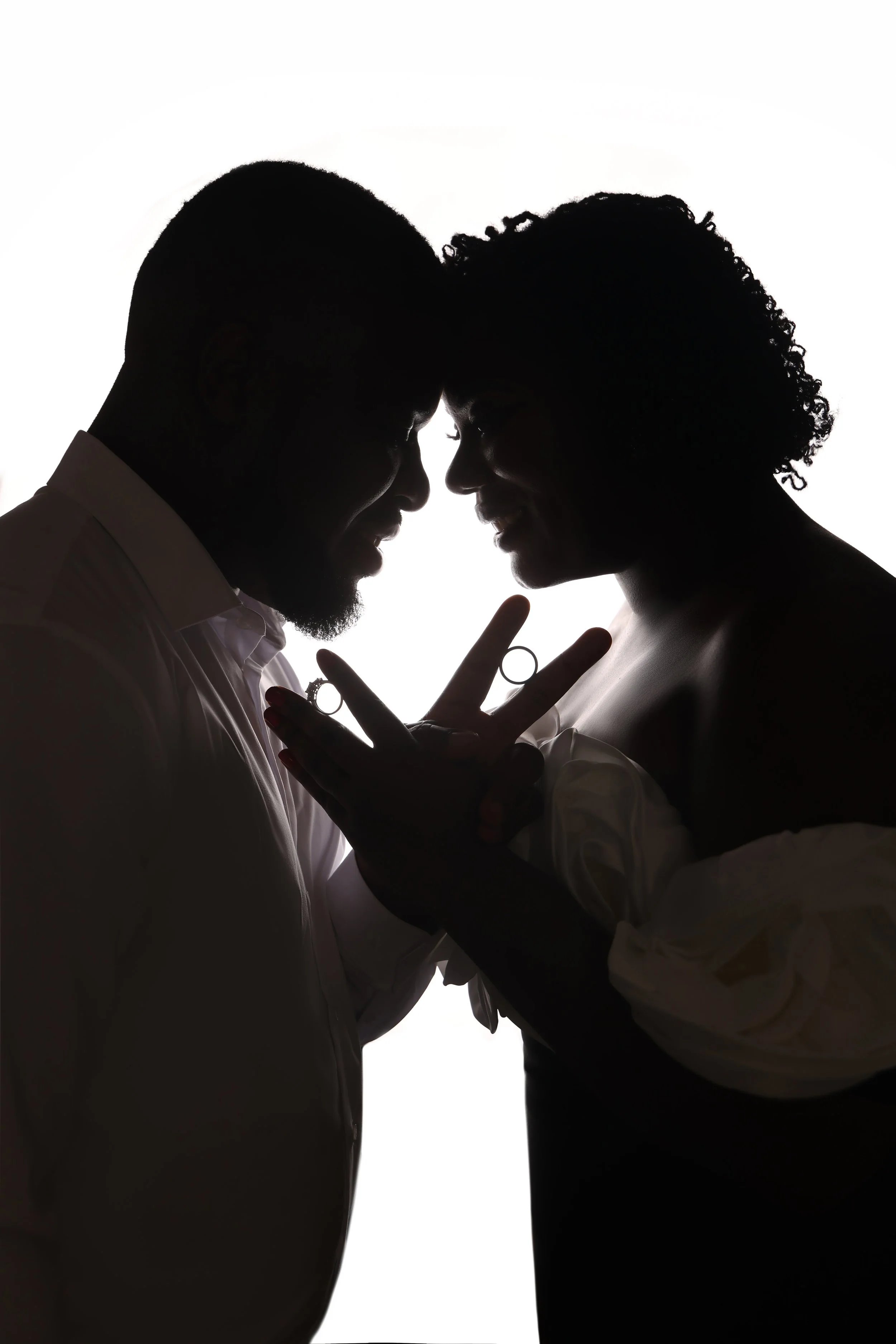 Silhouette of a couple facing each other close, with foreheads touching and hands clasped, against a white background