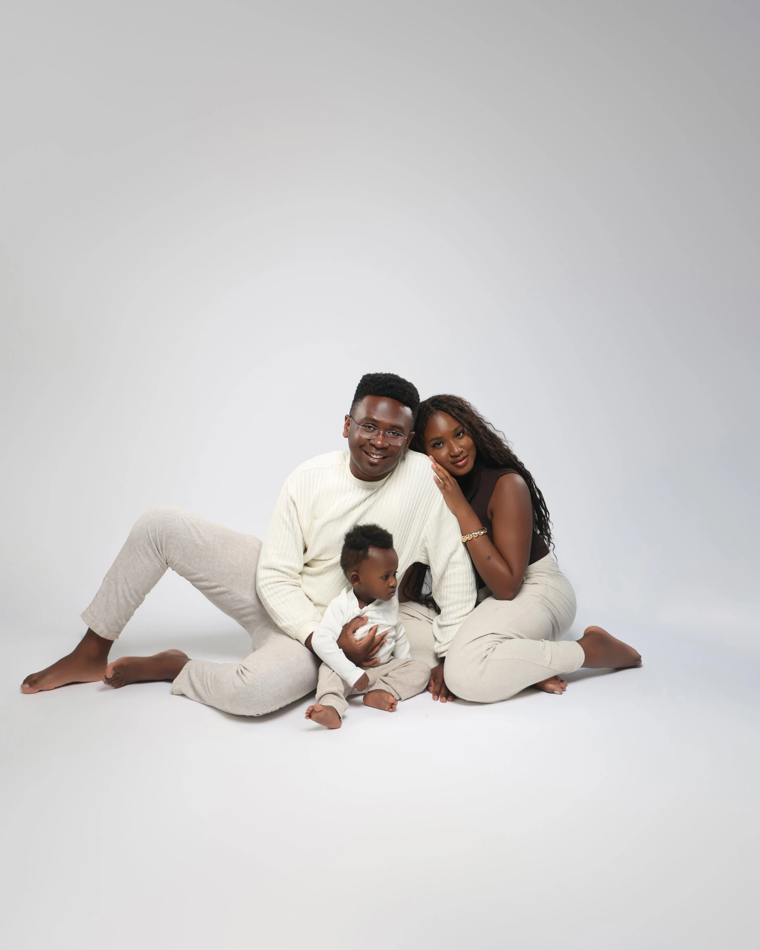 Family of three sitting together on the floor, smiling, in a studio with a neutral background.