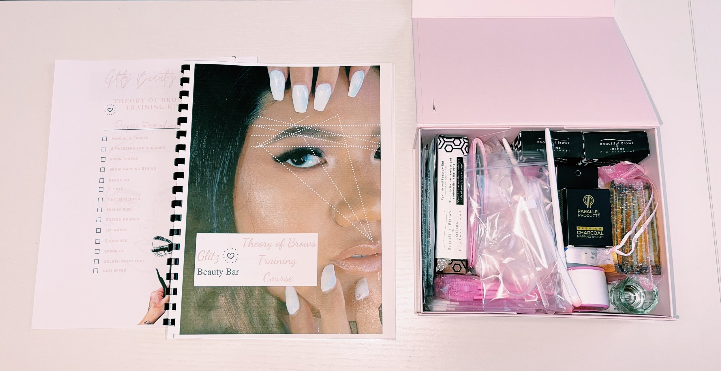 Beauty training course materials with a booklet and a kit containing nail and brow supplies on a white table.
