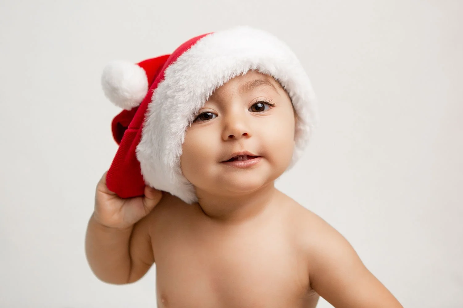 cute baby making an adorable face whlie trying to pull a Santa's hat off during a Christmas photoshoot in Cheltenham
