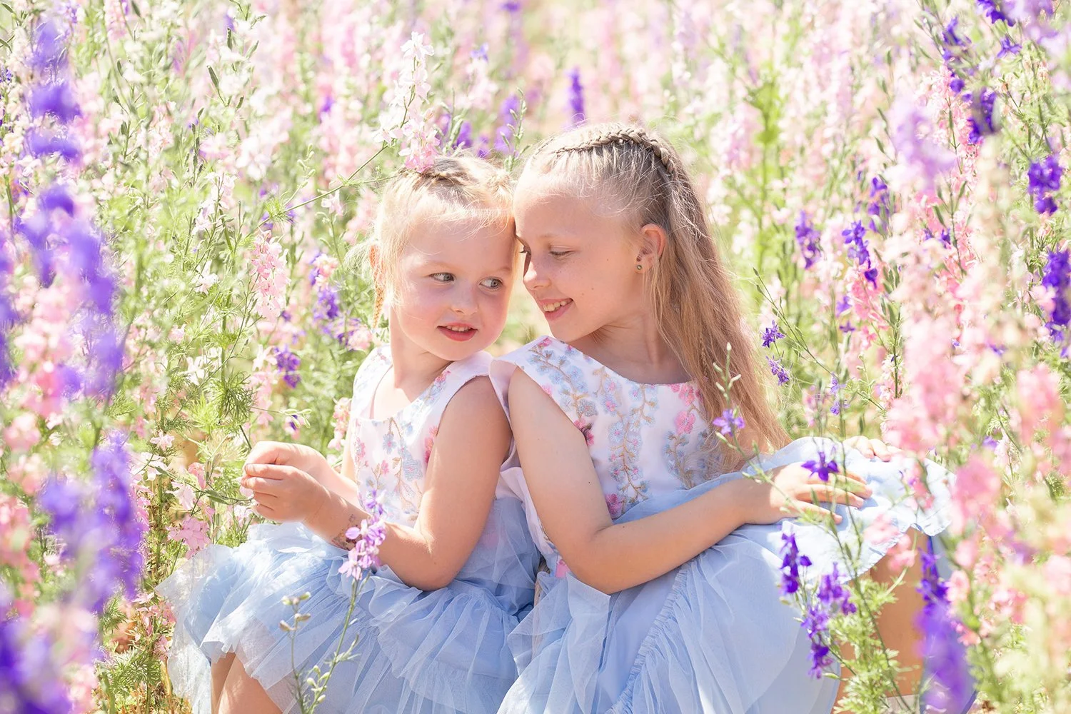 sisters in tulle dresses sitting in a confetti flower field during a family photoshoot in Wyke Manor