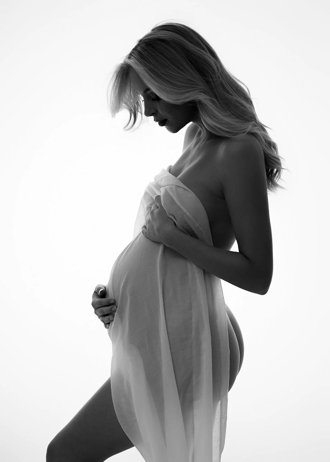 Pregnant woman in a simple fabric draping around her bump standing in a Cheltenham photography studio during a maternity photoshoot