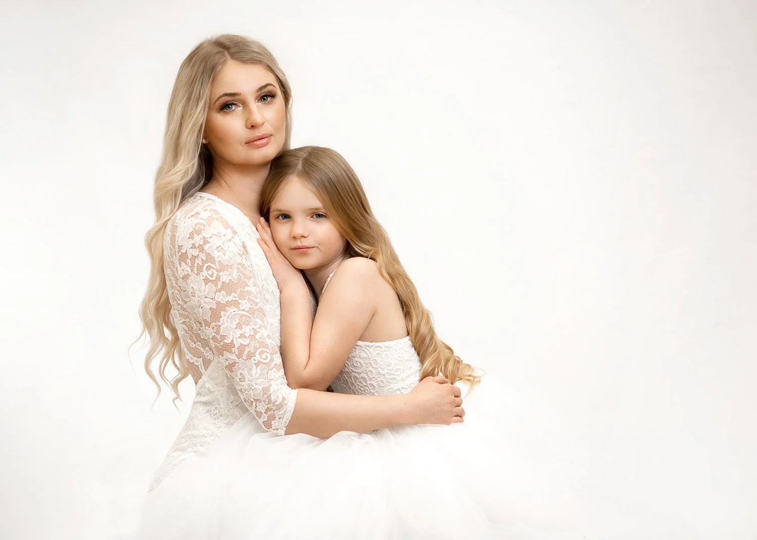 mum and daughter dressed in white lace dresses sitting together and cuddling during a photoshoot with Magda O Photography in Cheltenham, Cotswolds