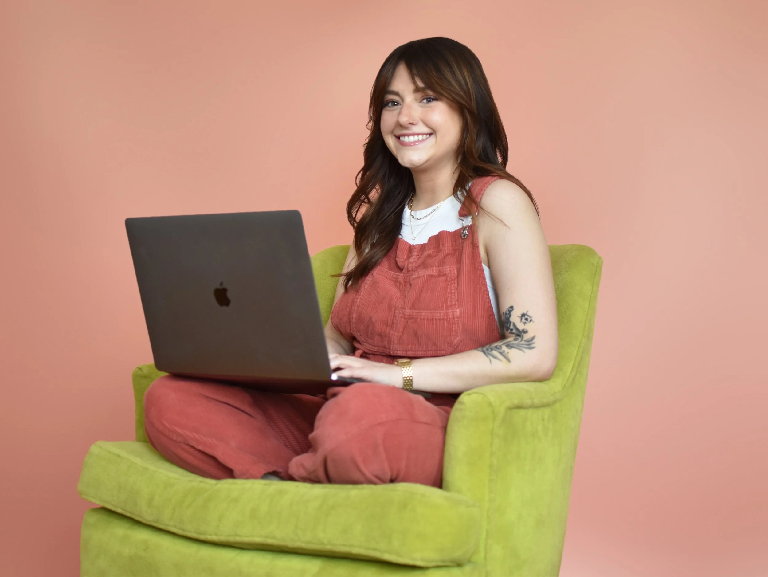 Julia Catalanello, a girl with brown hair, sit in a green chair with her laptop over crossed legs.