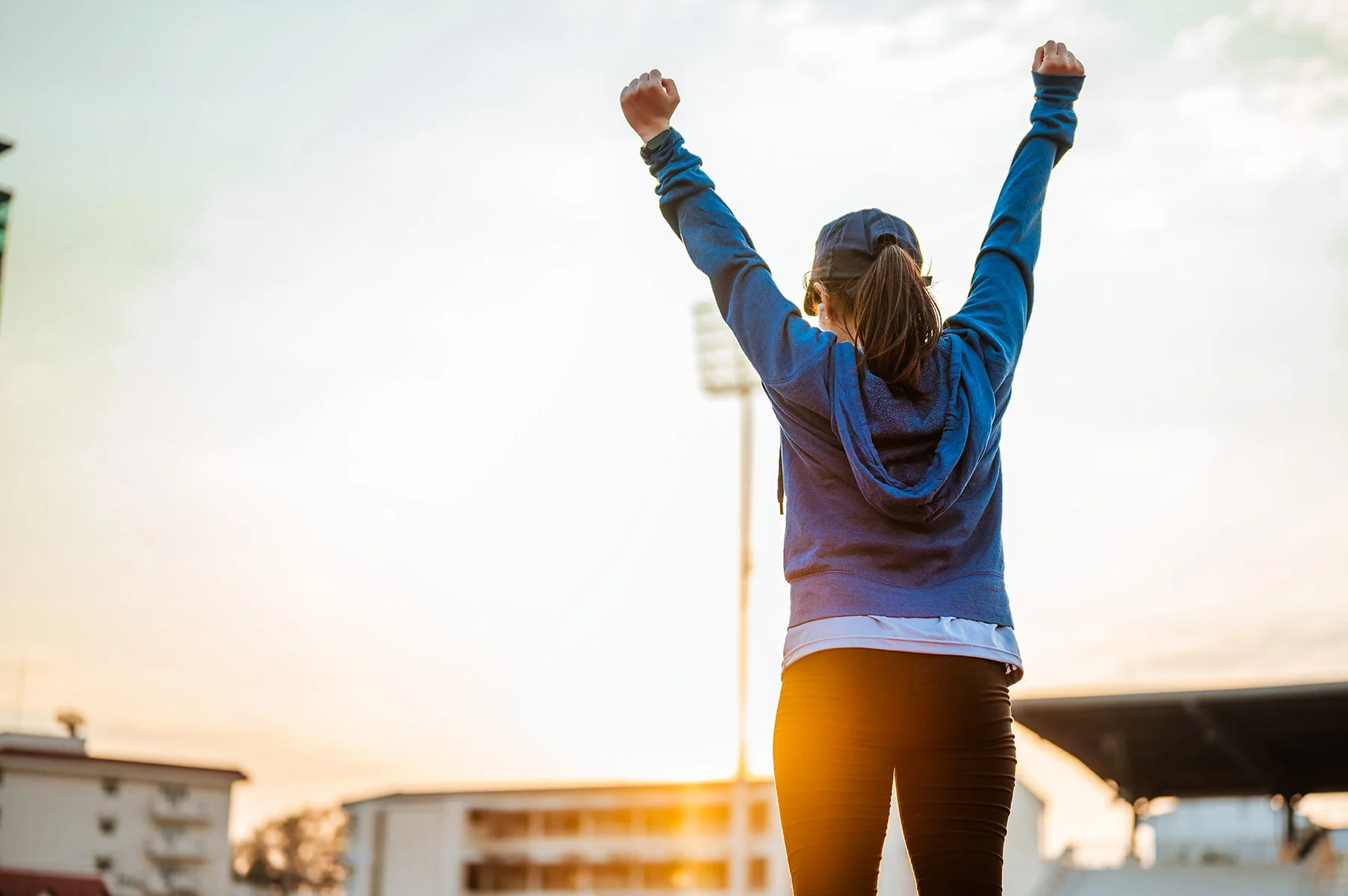 A woman standing outdoors at sunrise with her arms raised in the air, symbolizing strength, intention, and a positive mindset.