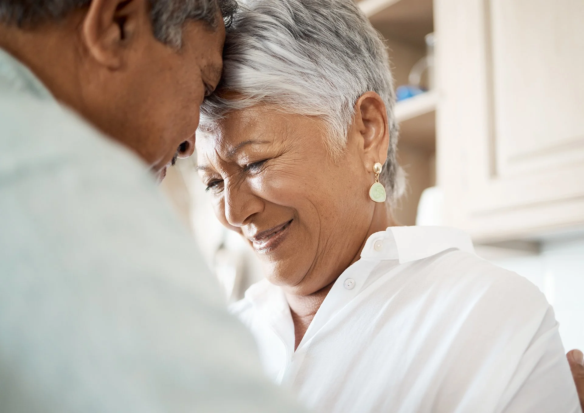 An older couple embraces while sharing a quiet, emotional moment at home.