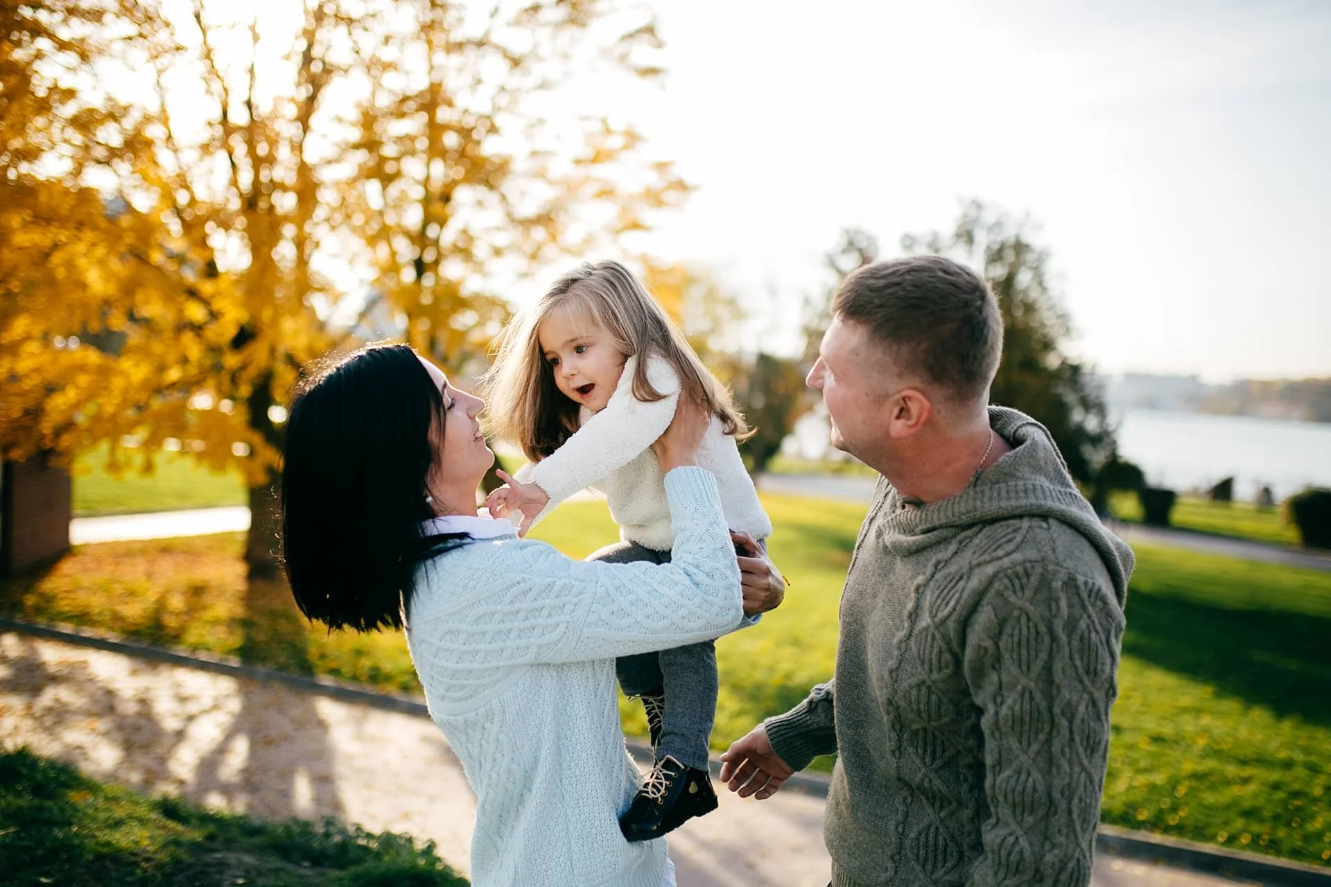 Parents spending time with their young daughter outdoors, sharing a joyful moment together in a park.