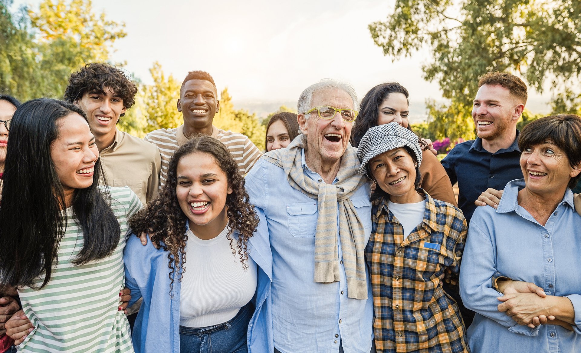 Multi-generational group of family and friends smiling together outdoors, representing the power of shared support and community.