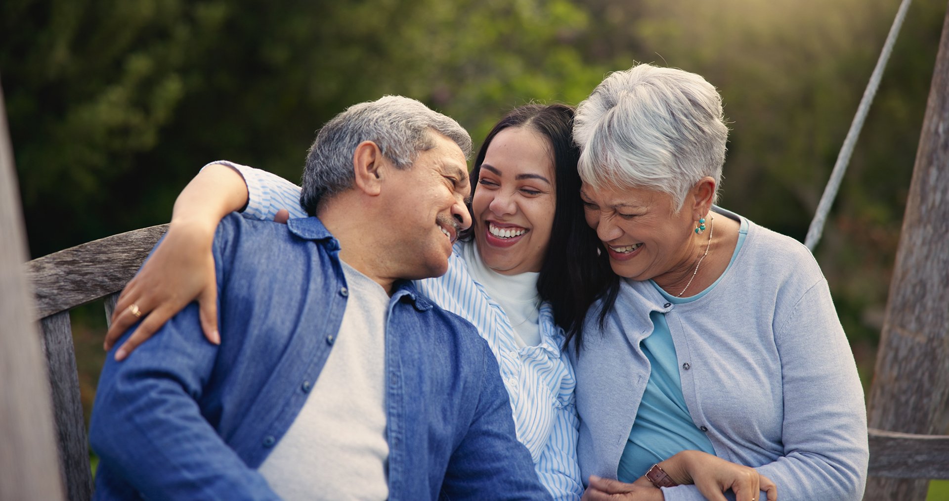 An adult daughter shares a joyful moment with two older adults on an outdoor bench, reflecting the importance of connection and time together.