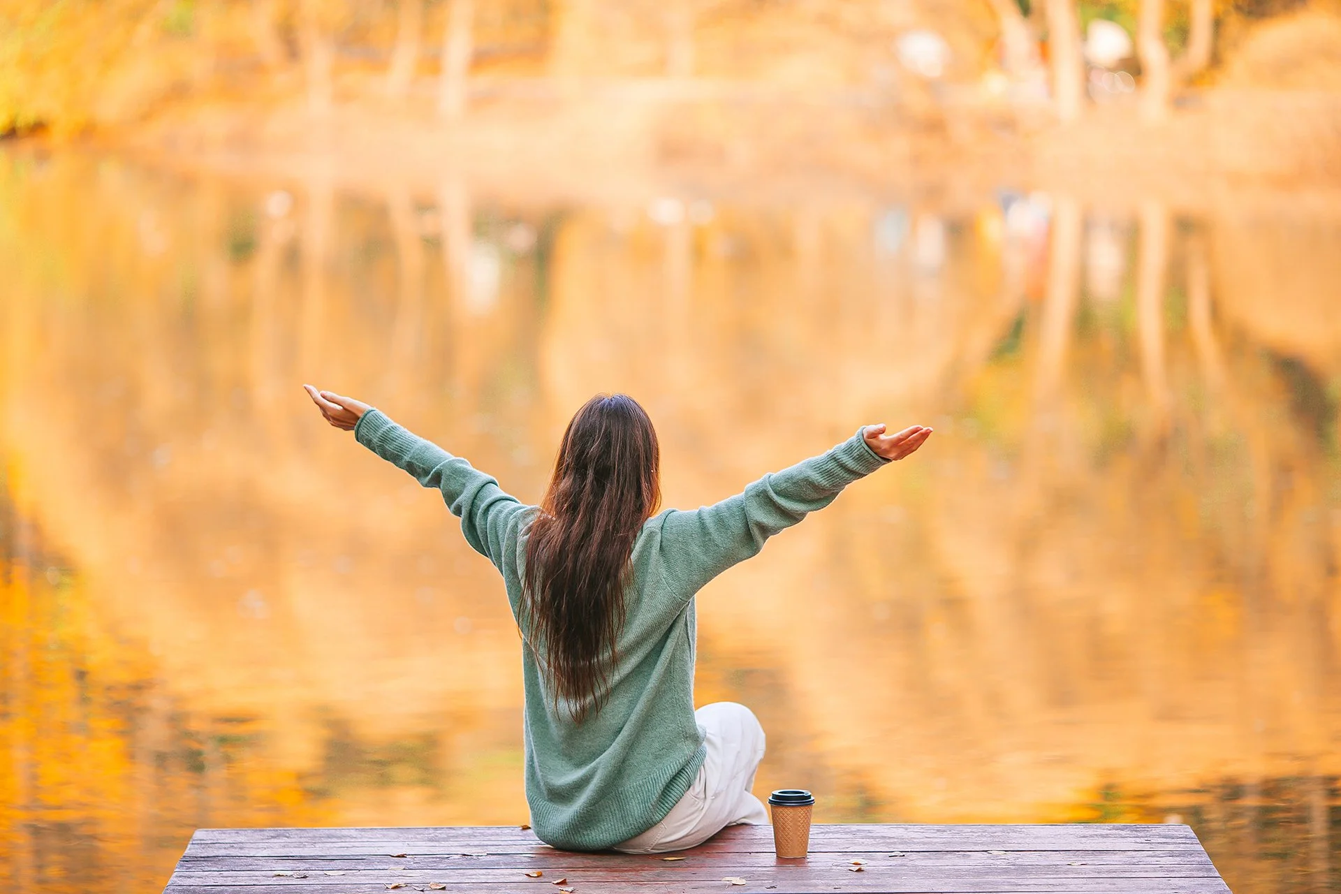 Person reflecting beside a peaceful lake at sunrise, representing positive thinking, personal growth, and a hopeful outlook.