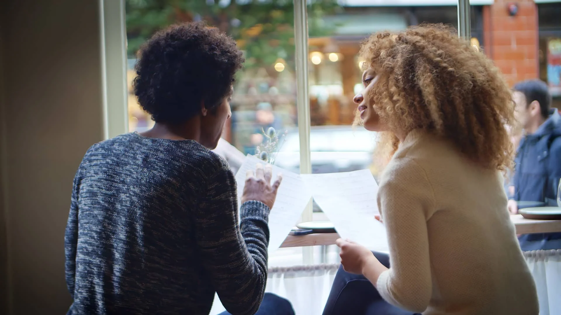 Two people sitting by a window talking in a café.