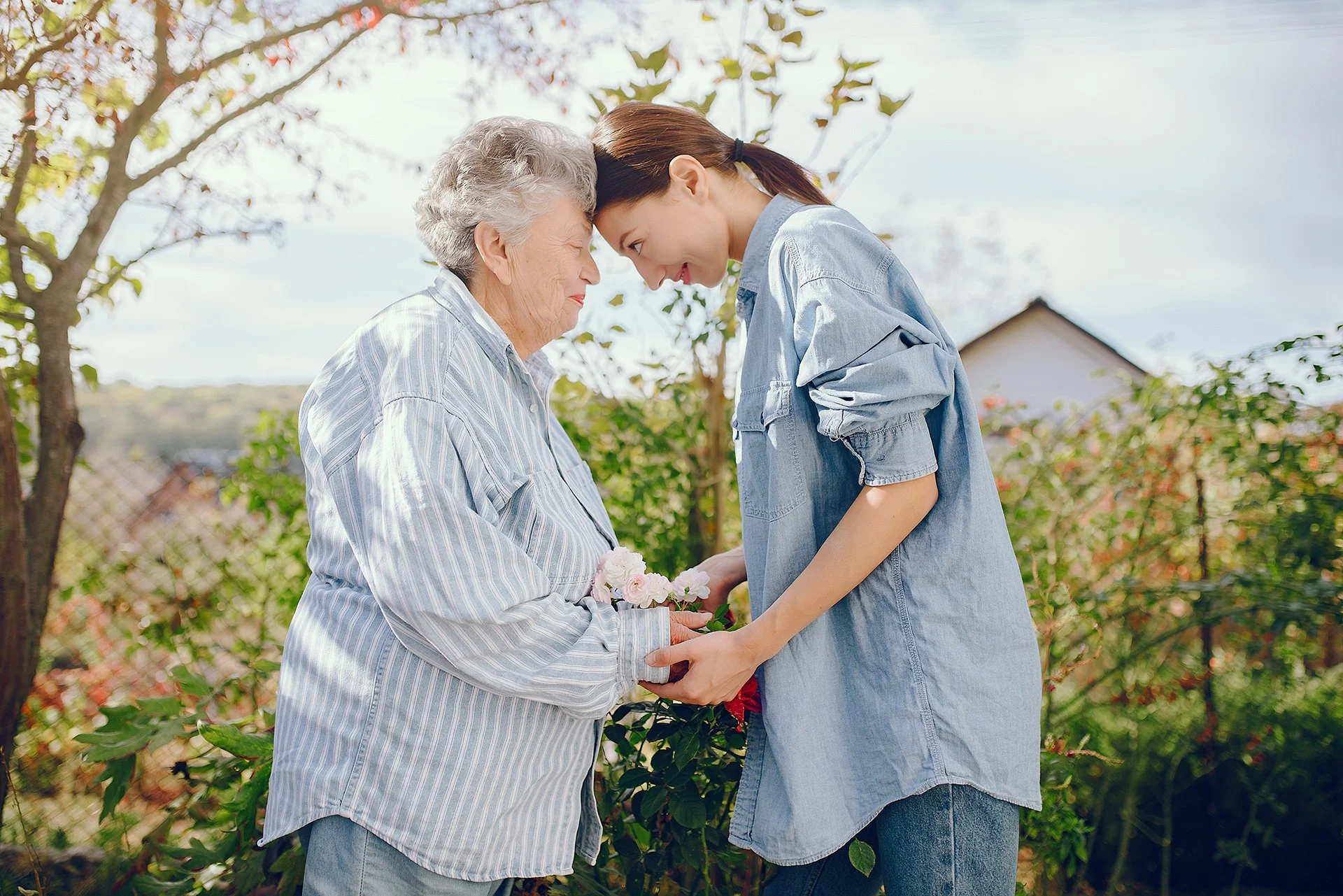 Young caregiver and older woman sharing a quiet, supportive moment together while tending flowers in a garden.