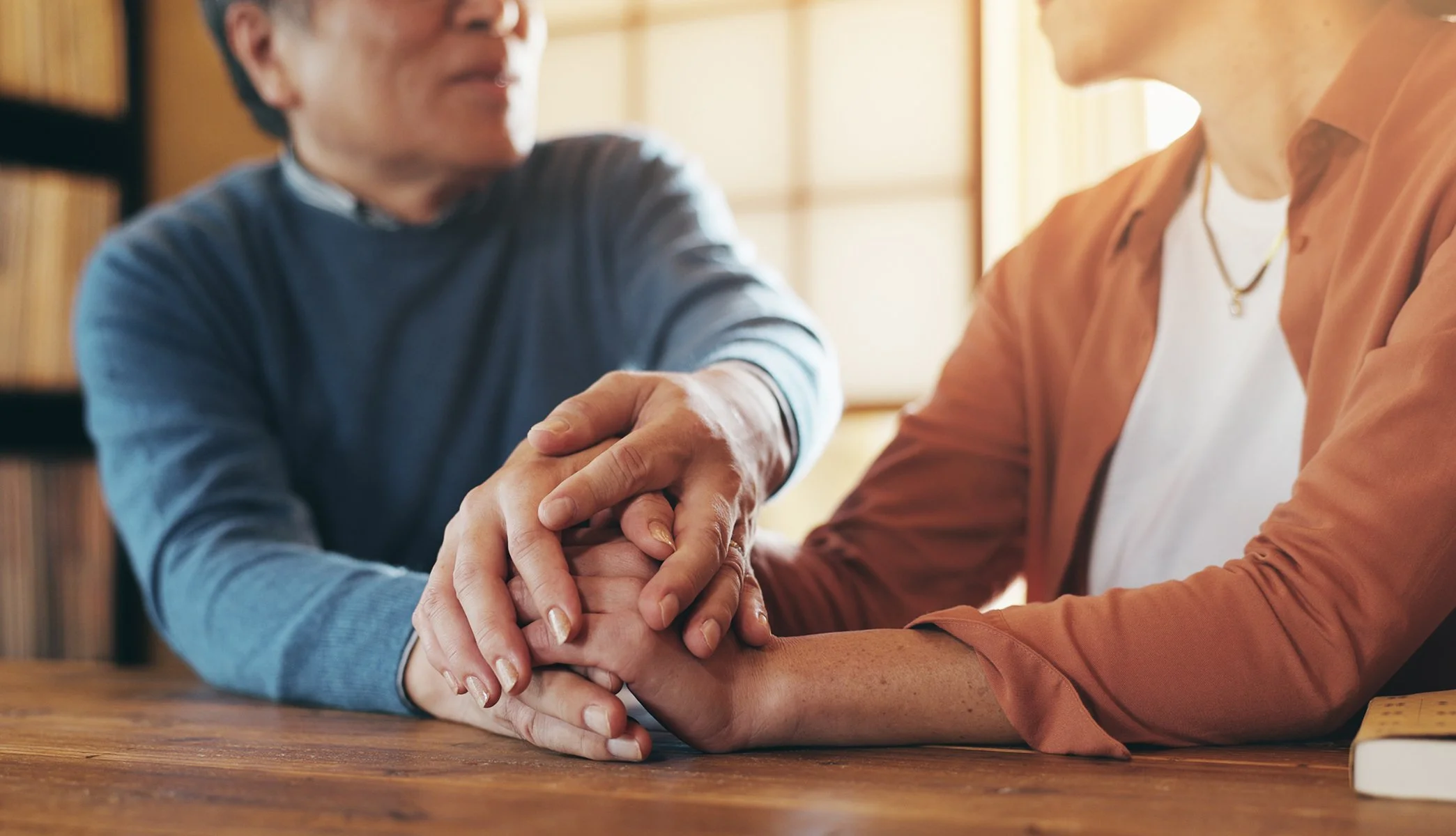 Two people sitting across from each other, holding hands in a moment of emotional support and connection.
