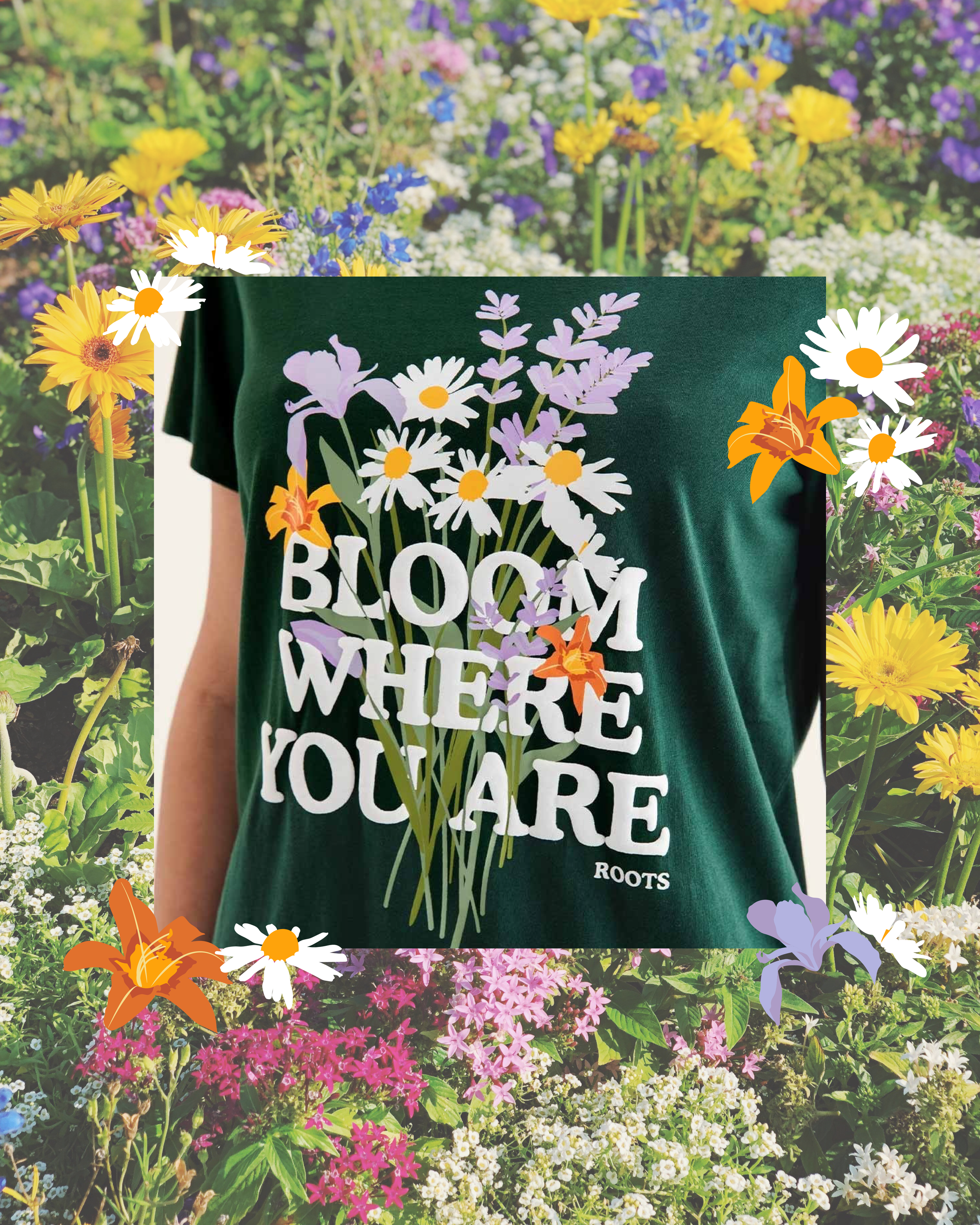 Person wearing a dark green shirt with a floral print and the words 'Blooms Where You Are Planted' printed on it, standing in front of a garden full of colorful flowers including daisies, lilies, and other blooms.