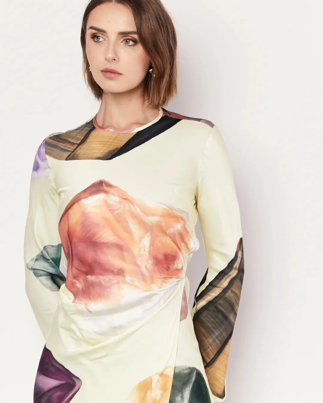 A woman with short brown hair wearing a long-sleeved dress with a colorful, abstract pattern.