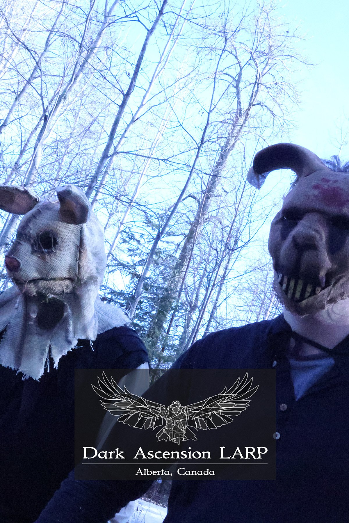 Two people wearing animal masks, one resembling a goat and the other a ram, outdoors in a wintery forest with bare trees. Overlayed text reads 'Dark Ascension LARP, Alberta, Canada.'