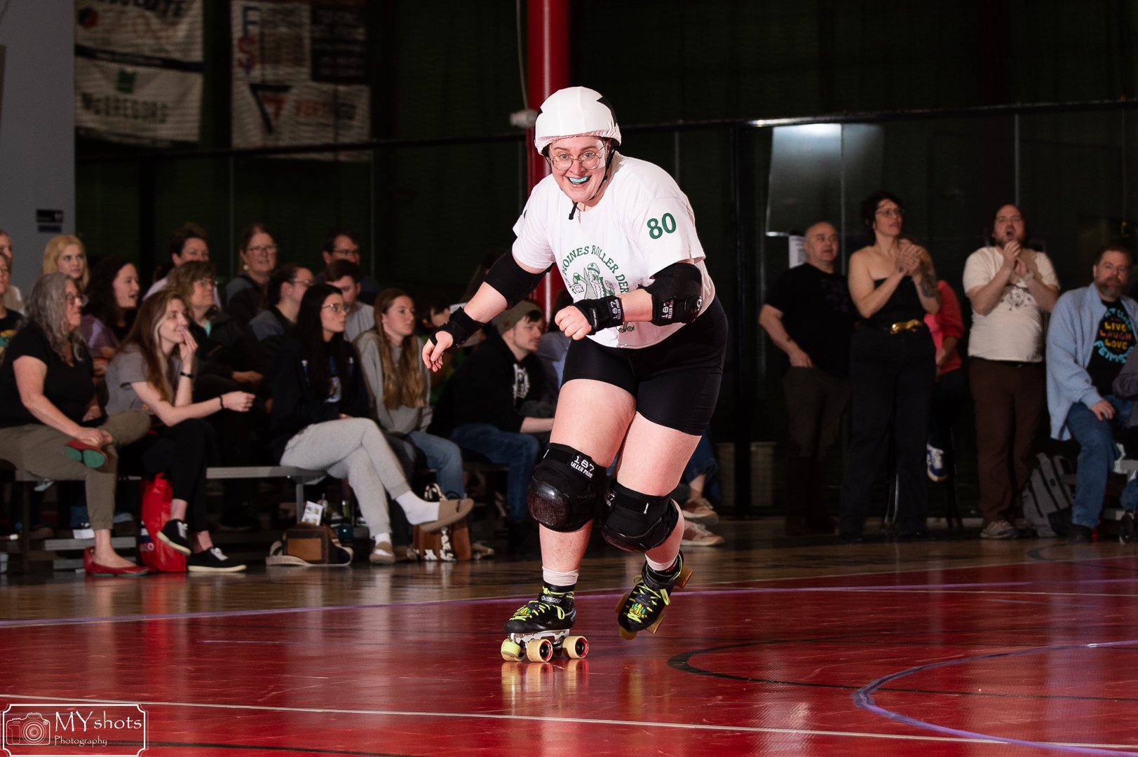 Headshot of Skatie wearing large, round glasses softly smiling in a DMRD jersey. smiling