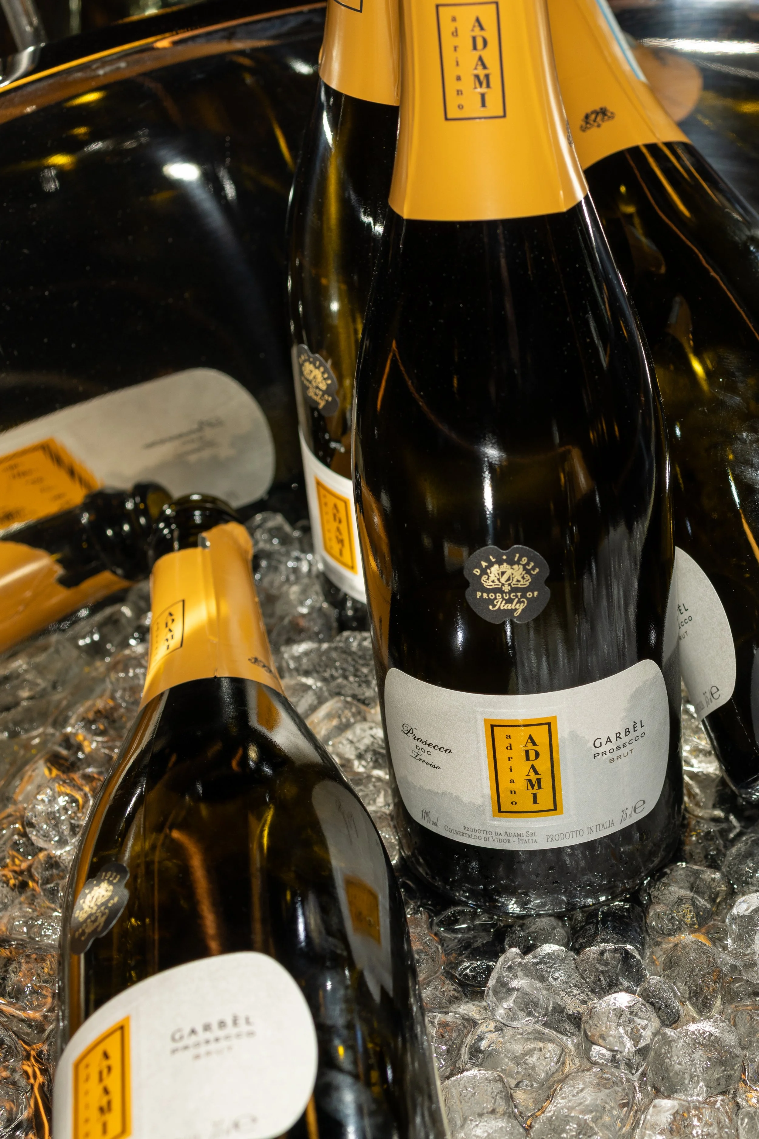 Several bottles of Adami Prosecco sparkling wine in a bed of ice, with yellow and black labels visible.