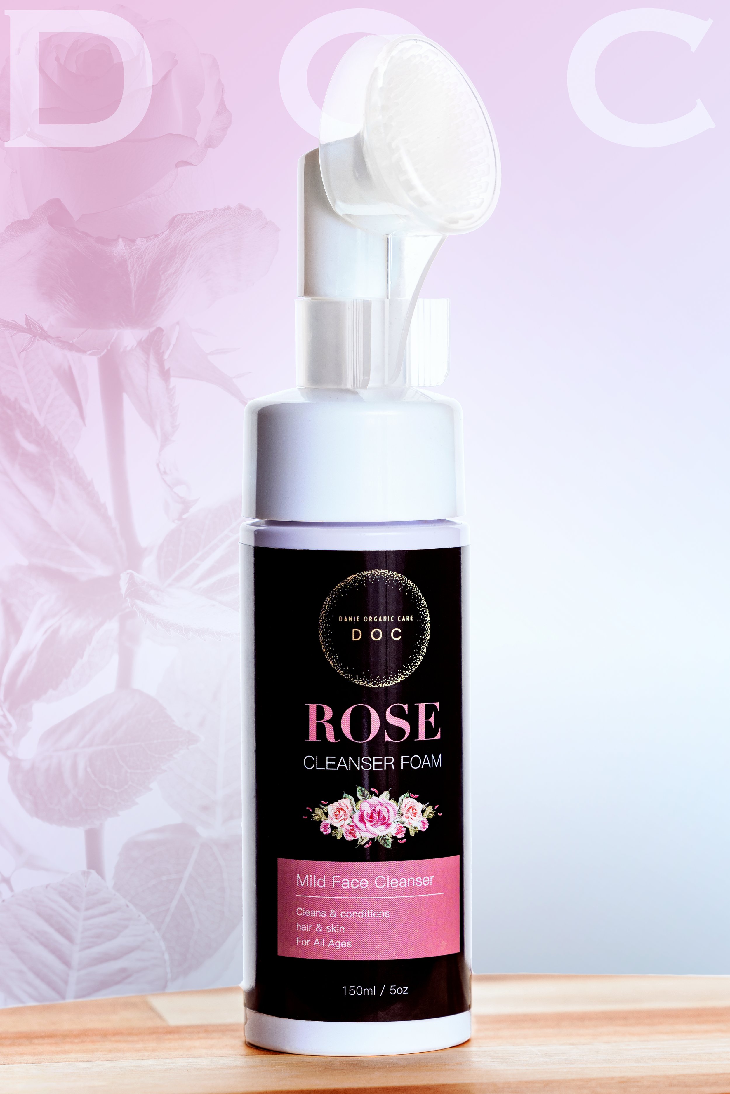 A white bottle of Danie Organic Care Rose Cleanser Foam on a wooden surface with a pink and white background featuring floral and leaf designs.