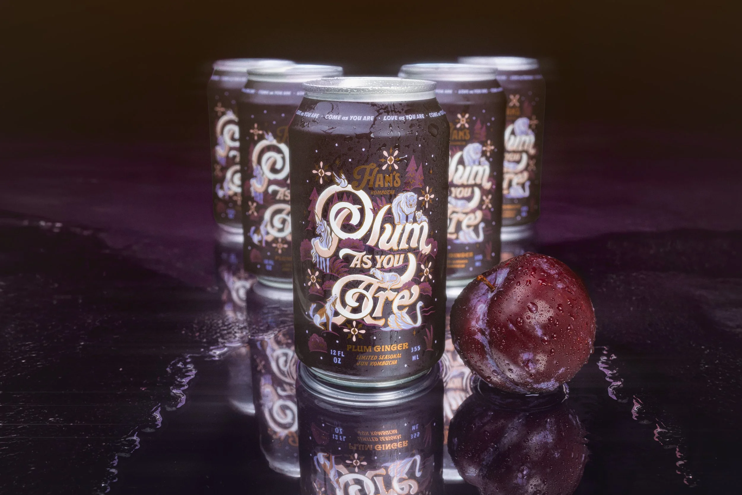 Six cans of Plum Ginger flavored kombucha called 'Plumb As You Are' arranged in a semi-circle on a dark reflective surface with a red plum fruit beside them, condensation on the cans and reflections on the surface.