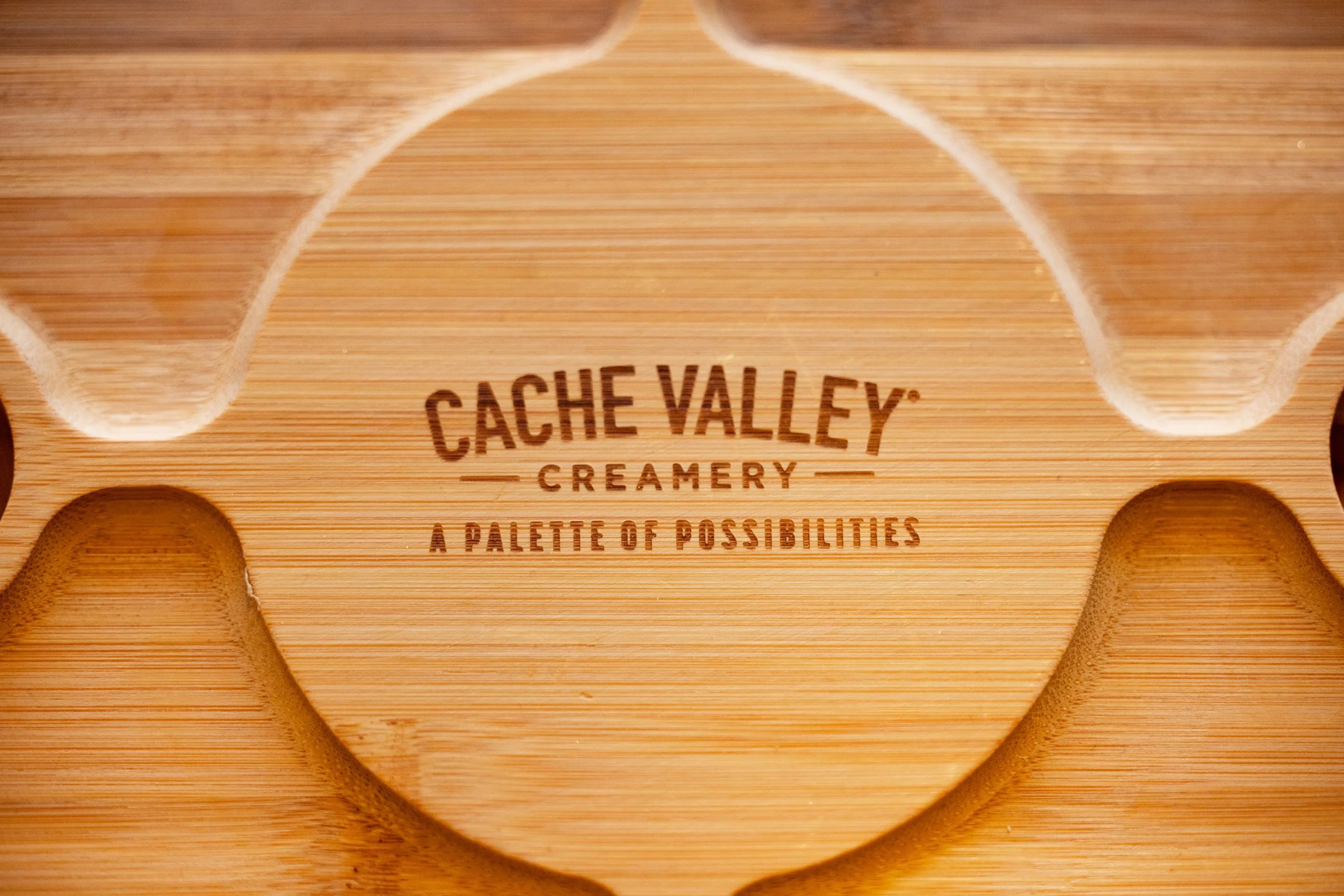 Close-up of a wooden box with the text "Cache Valley Creamery" and "A Palette of Possibilities" printed on it, featuring circular cut-outs and a minimalist design.