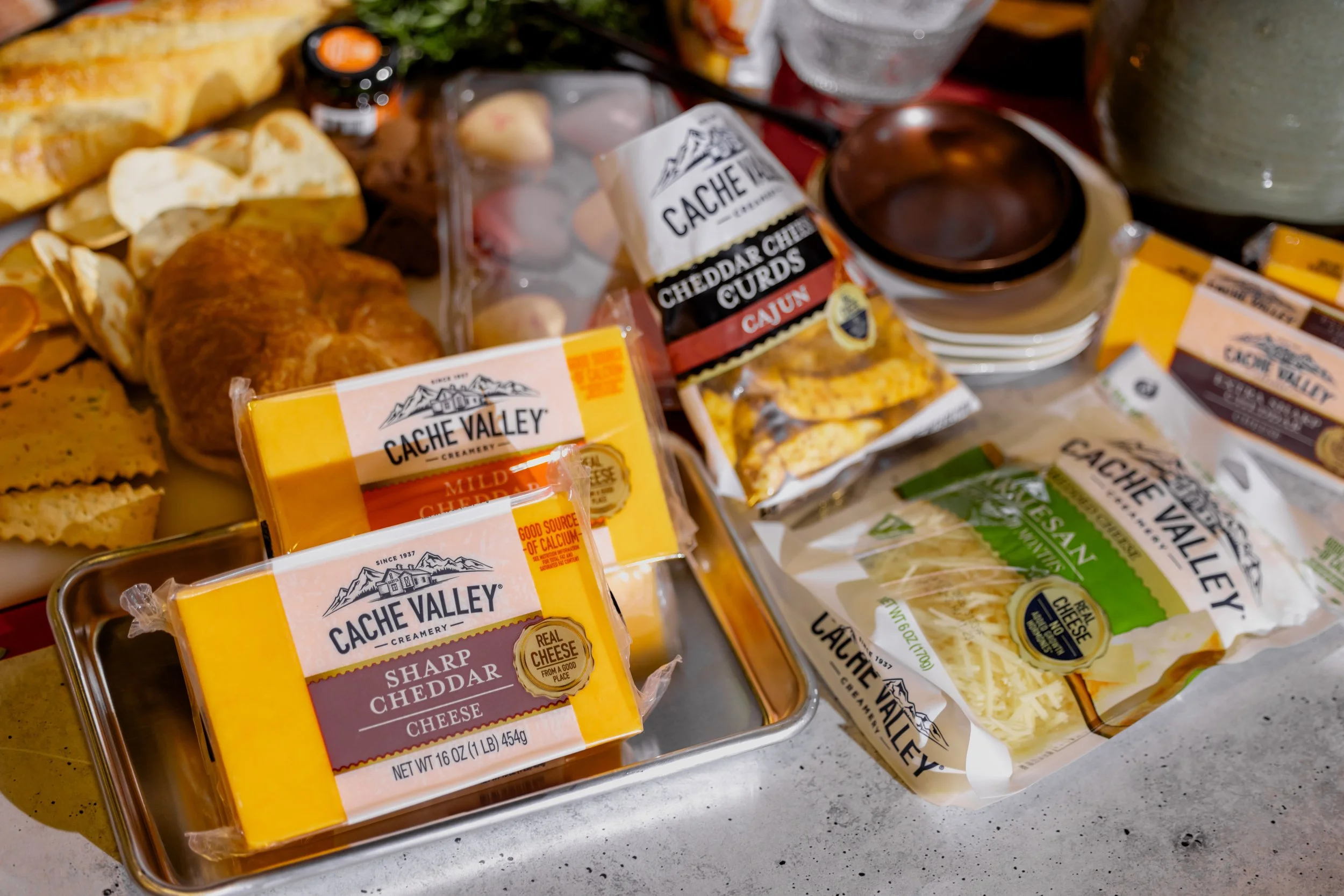 Assorted cheese packages, including sharp cheddar, mild cheddar, and vegan cheese, along with various deli meats, bread, and condiments on a table.